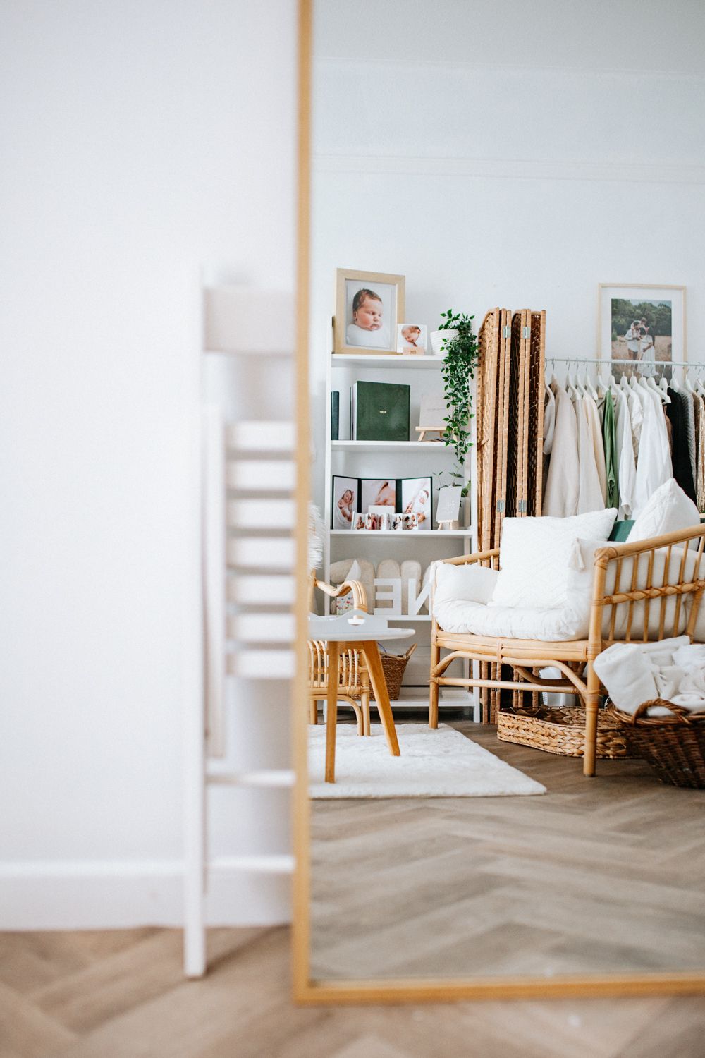 Modern bright interior with bamboo chair, white shelving unit, floor mirror and herringbone wood flooring in cozy bedroom.