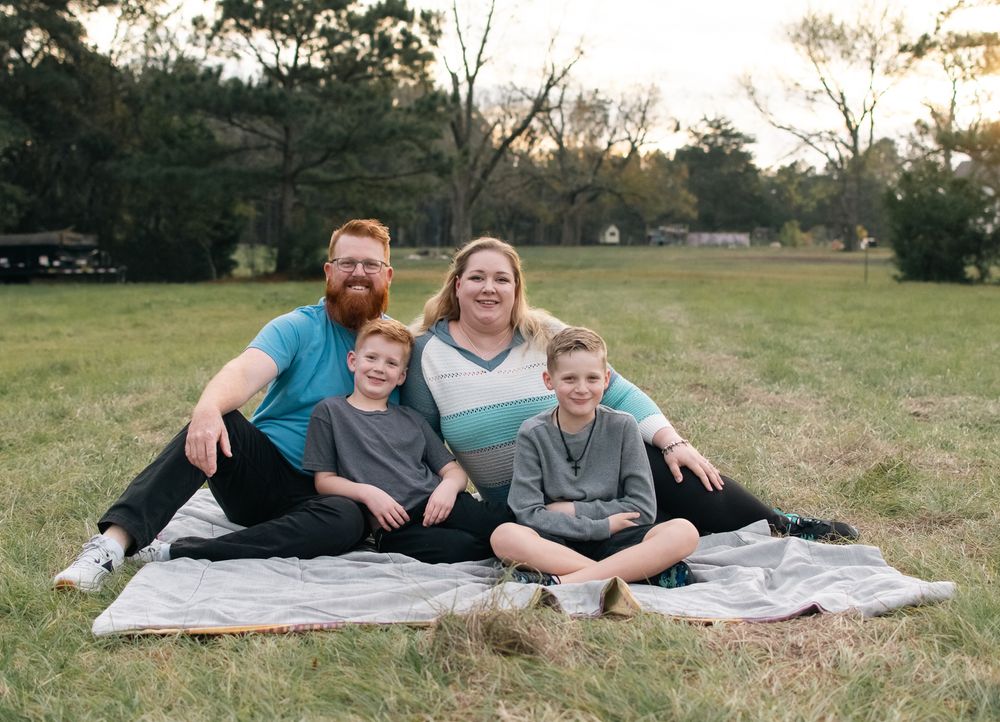 Family members relaxing together on a blanket in a grassy field at sunset.