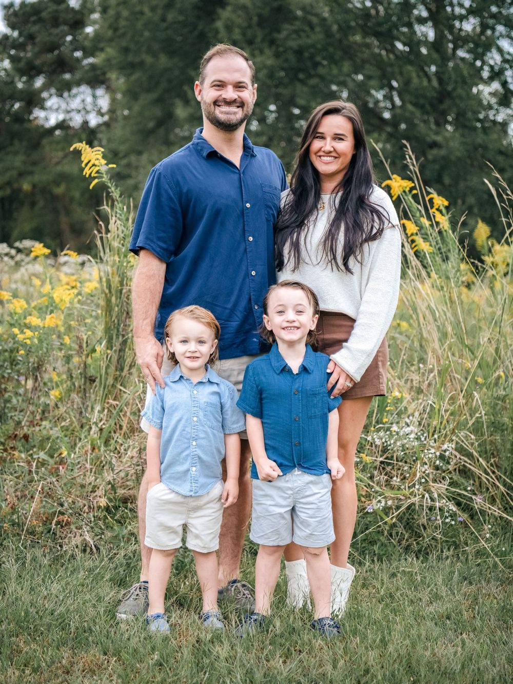 Family in coordinating blue and white outfits poses together in a field of wildflowers.