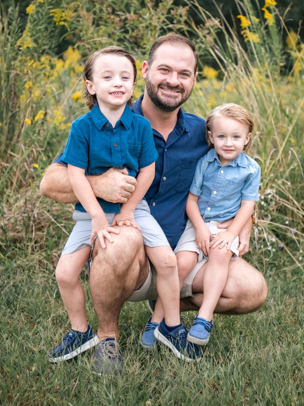 Family with young children smiling and sitting together in a summer meadow with yellow flowers.