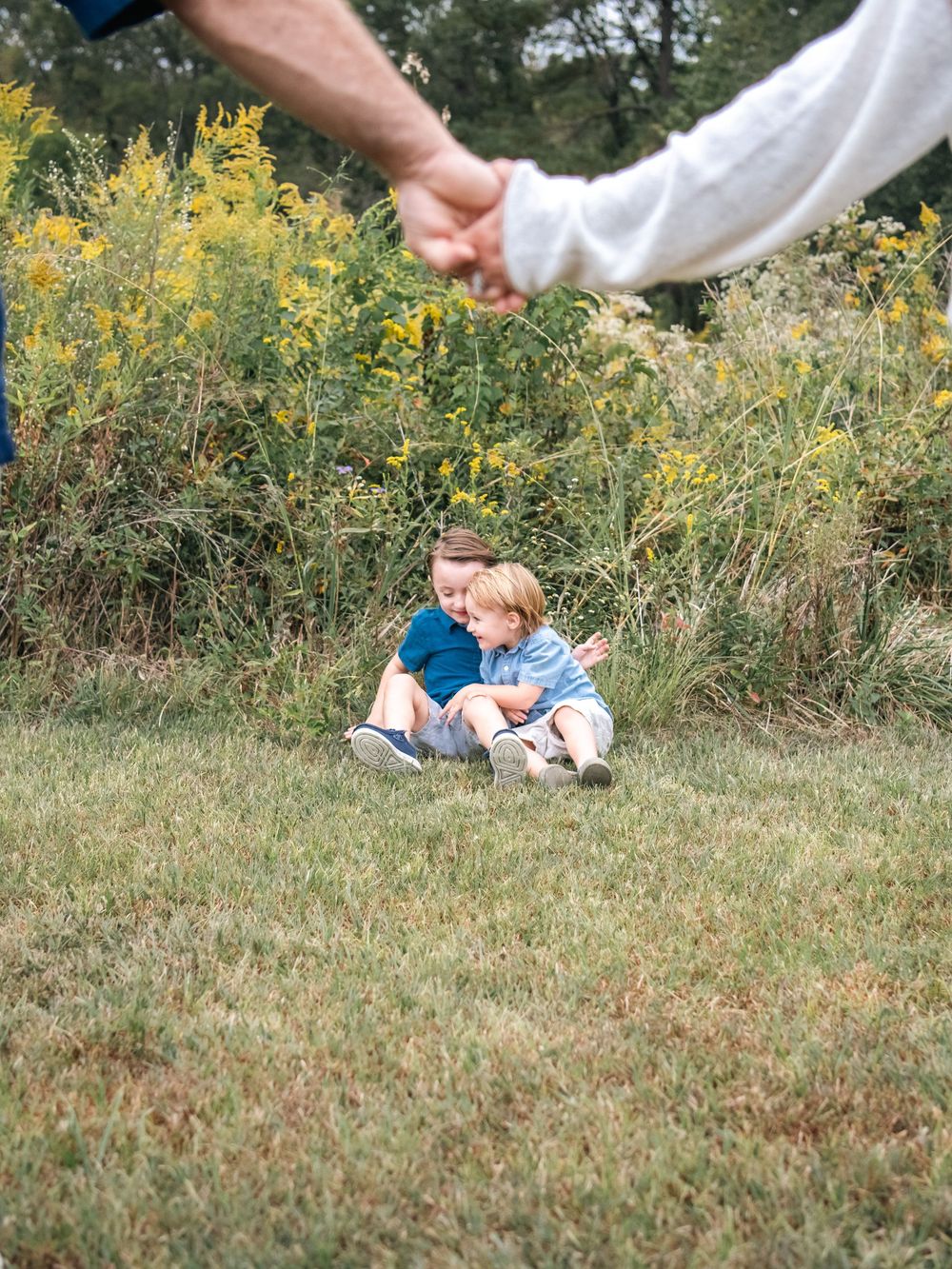 Family members playing and laying in grass during a relaxed outdoor photo session.