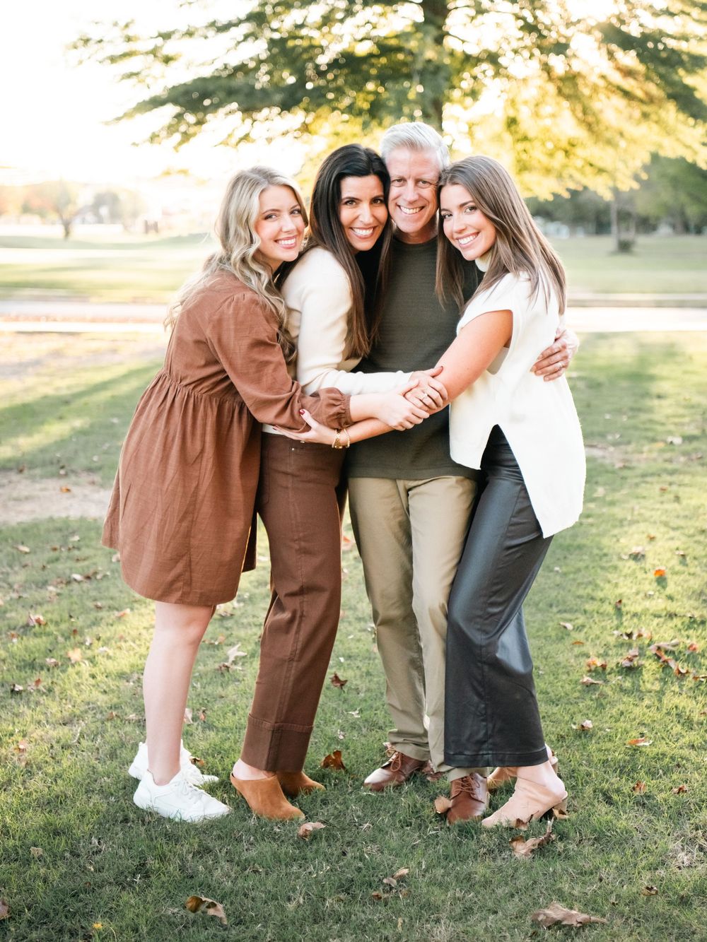 Four people pose playfully together outdoors in coordinated brown and neutral outfits during a golden sunset.