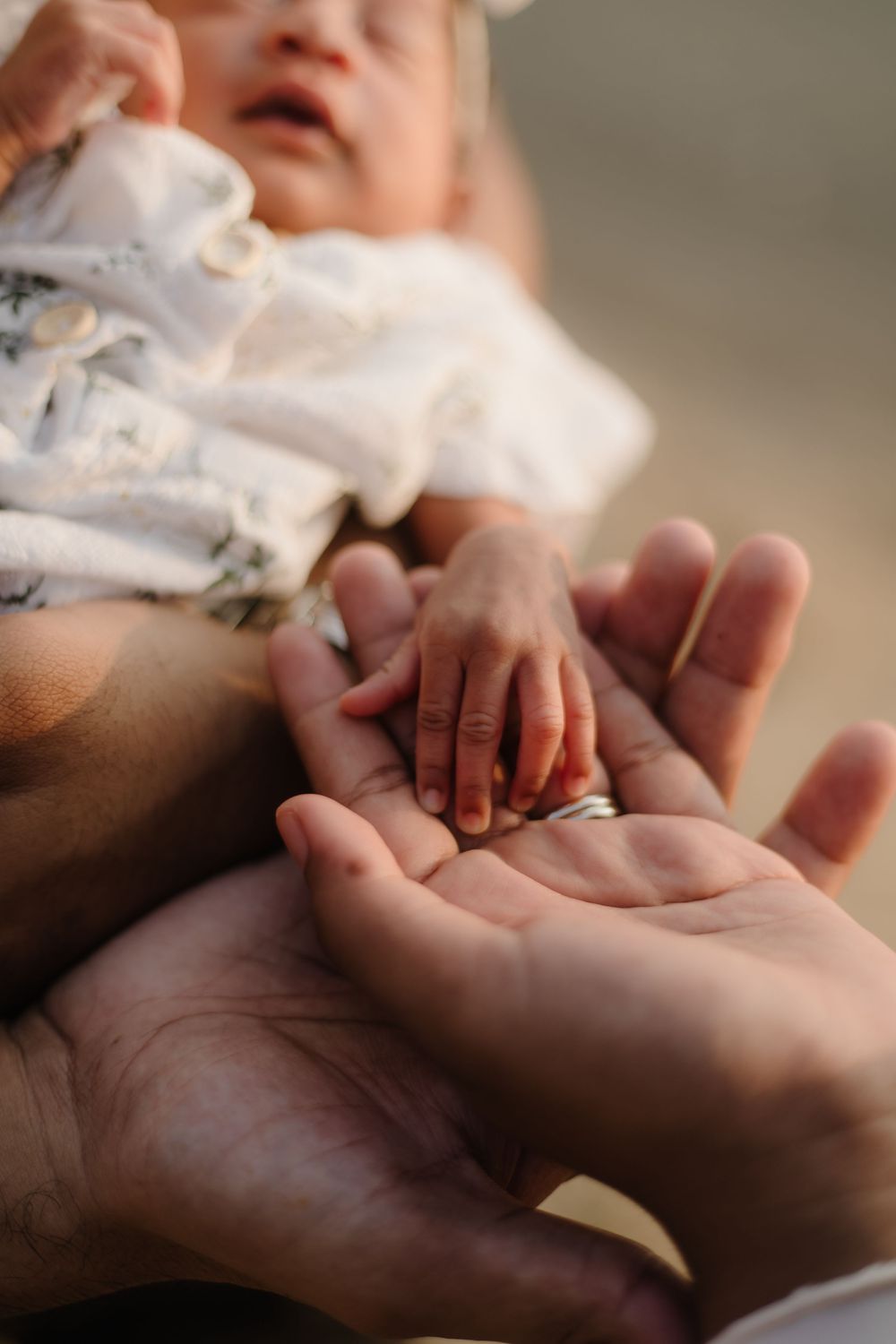 A newborn baby's tiny hand resting gently in an adult's open palm, with a wedding ring visible.