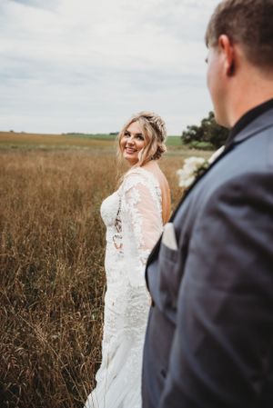 Elegant bride in lace dress poses in rustic field setting.