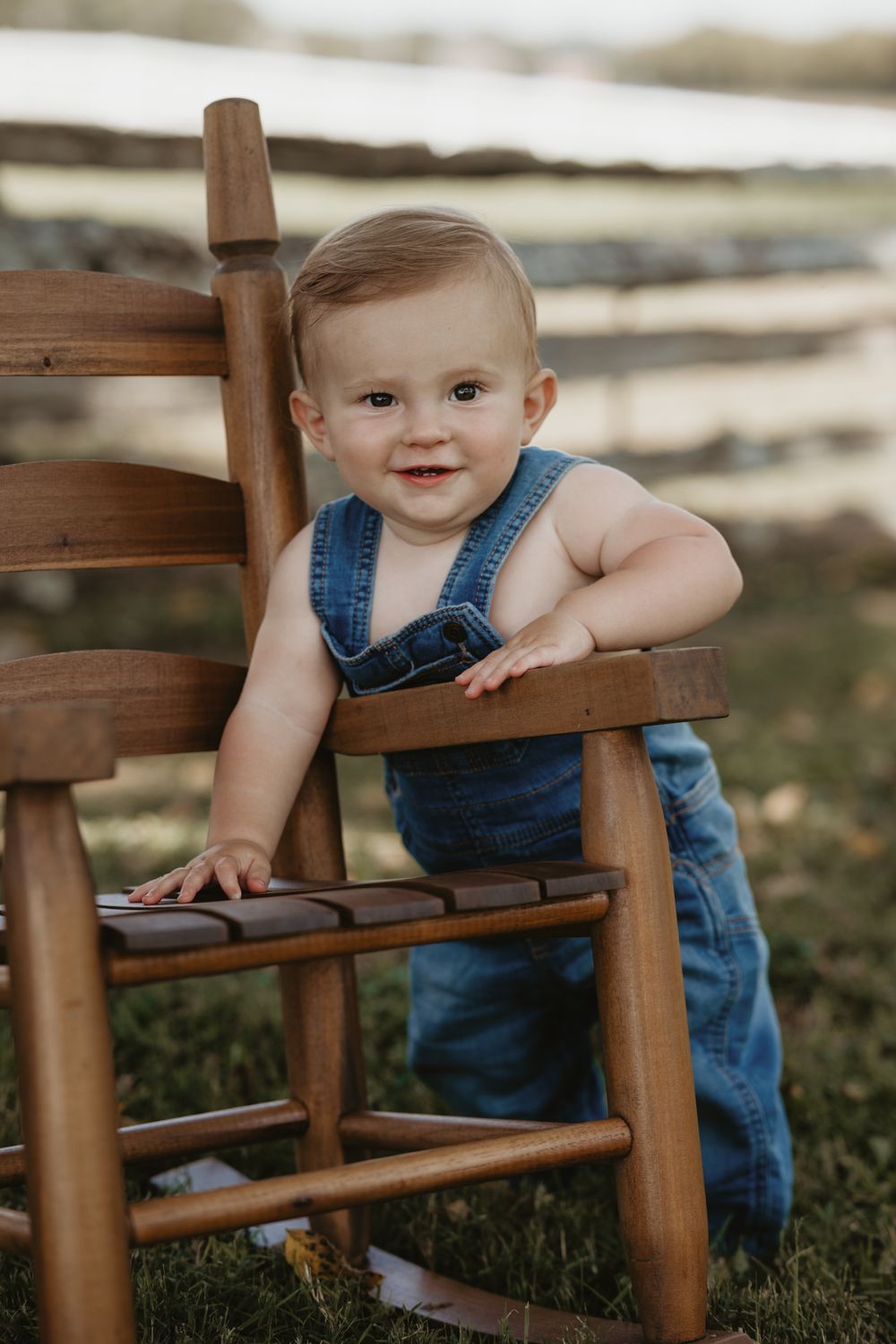 A small child in denim overalls plays around a wooden rocking chair on grass in a series of candid photos.