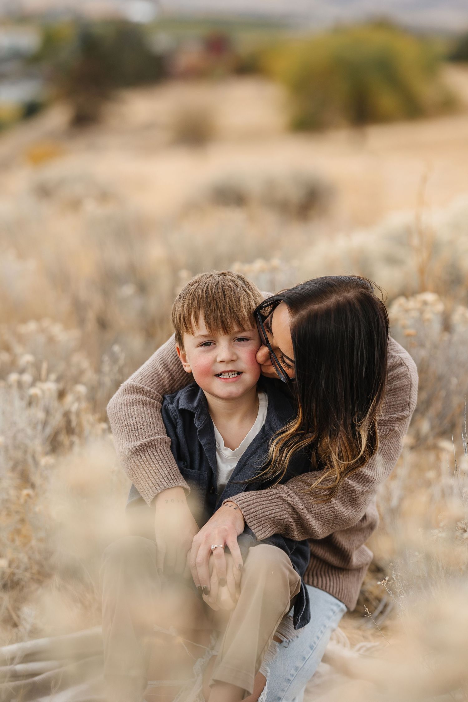 A tender moment shared between parent and child sitting together in a golden autumn field during sunset.