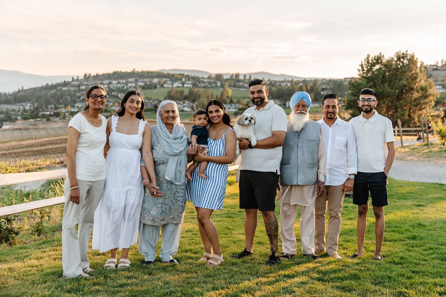 A group wearing coordinated white outfits poses together outdoors during golden hour at quails gate in west Kelowna during a family session