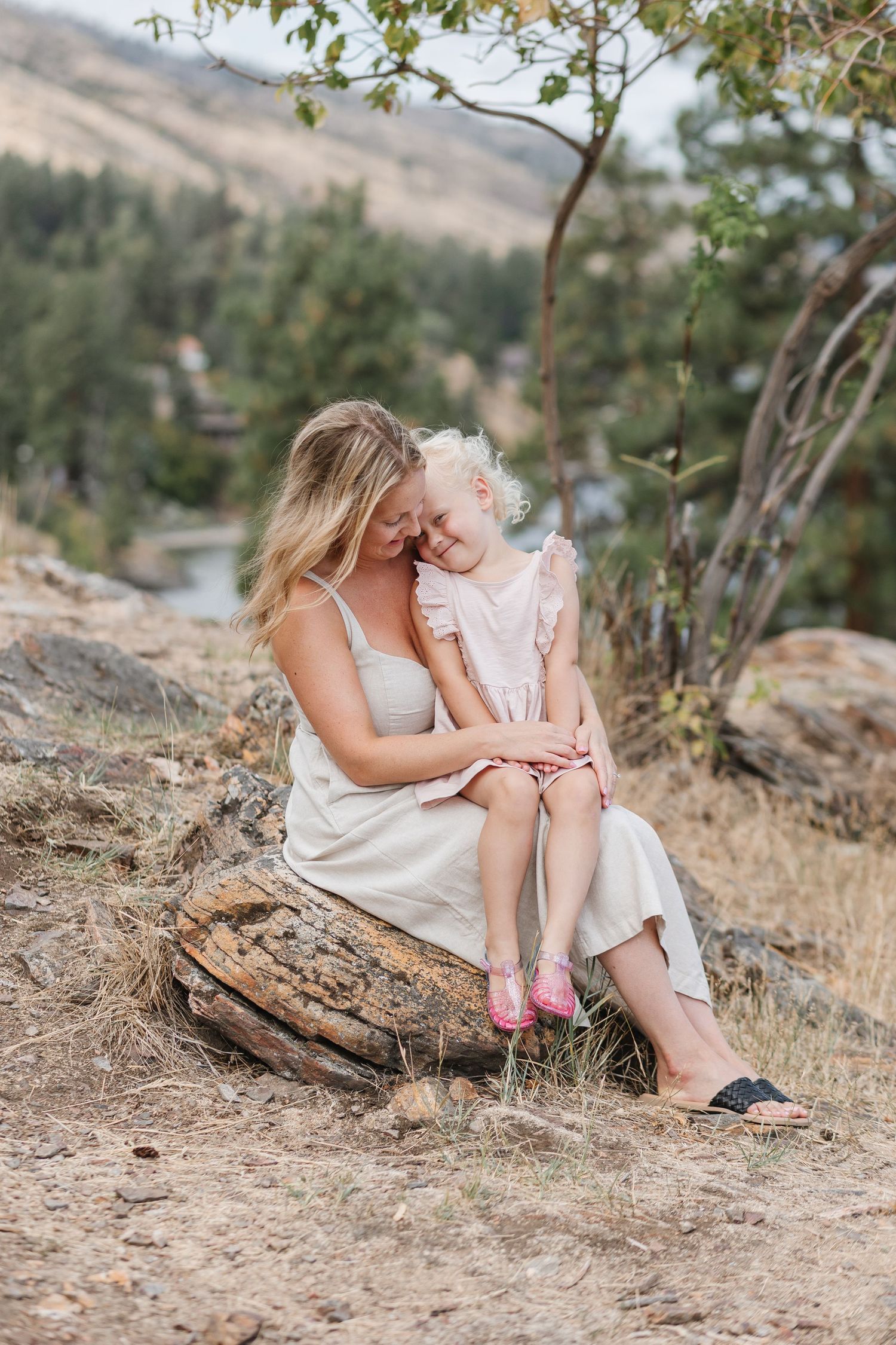 A tender moment between parent and child sitting on a rocky outcrop with mountains in the background.