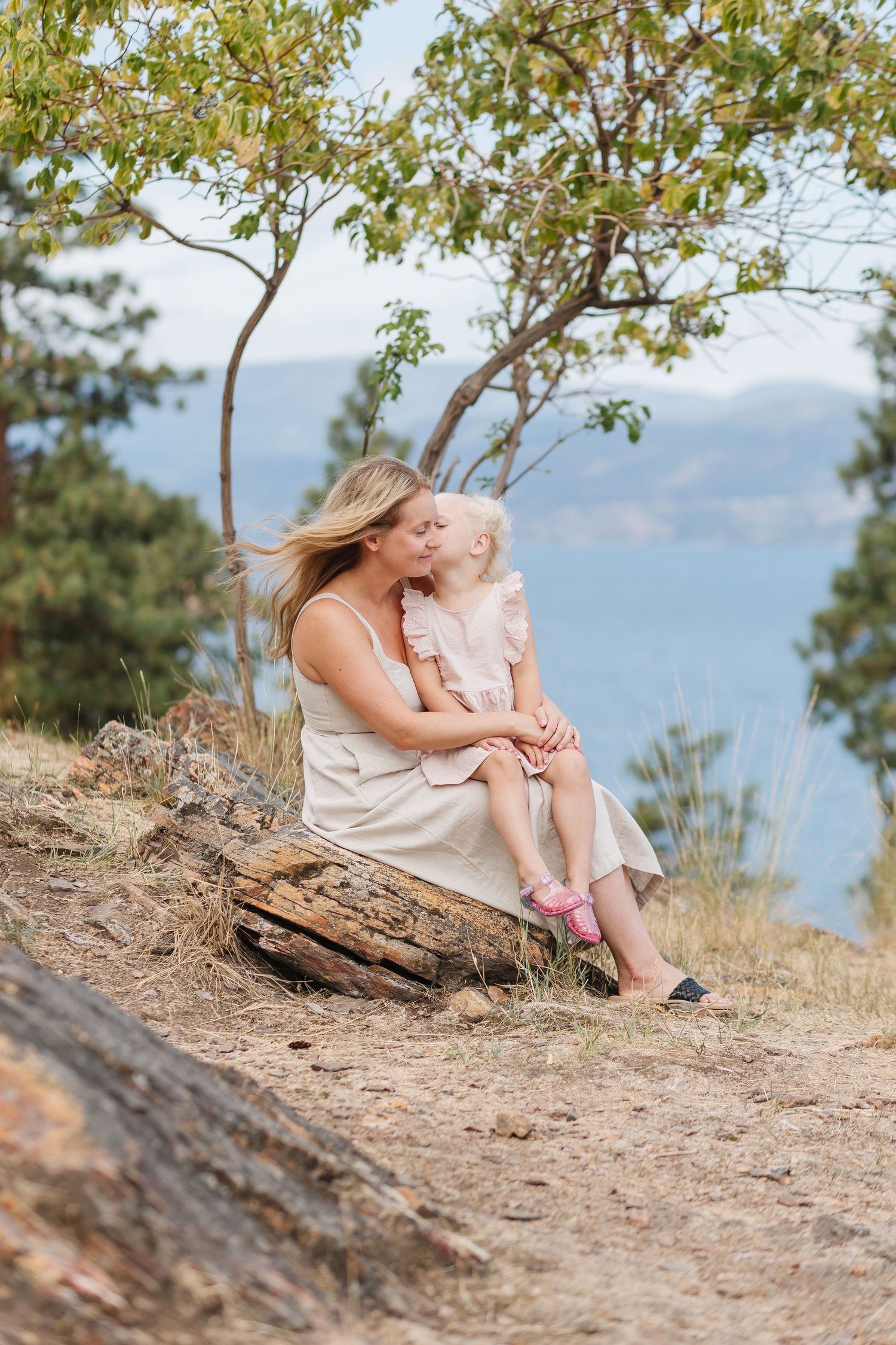 An intimate portrait of a parent and child sharing a loving moment on a clifftop overlooking a scenic vista.