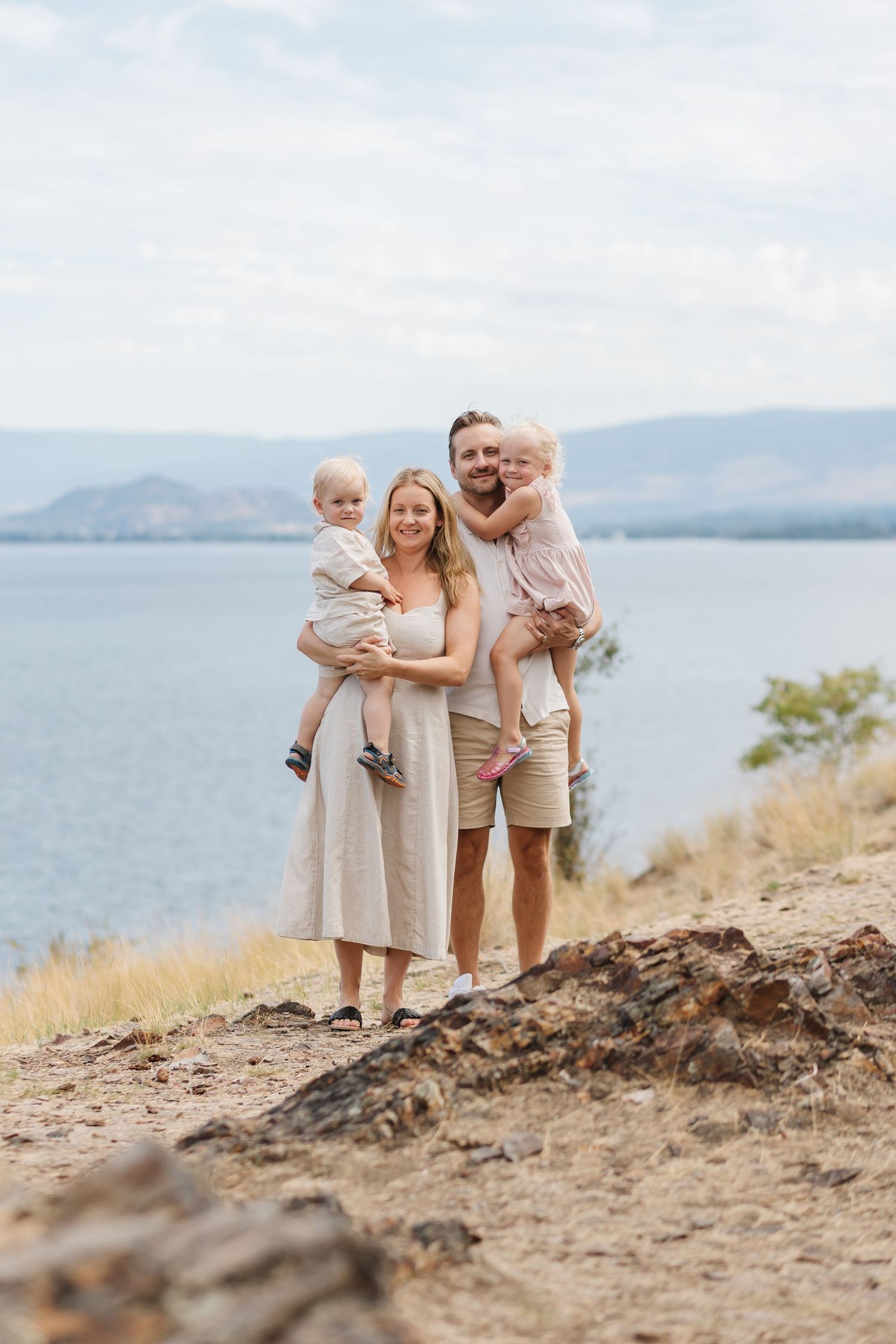 A family of four poses together on a scenic overlook with a lake and mountains in the background.