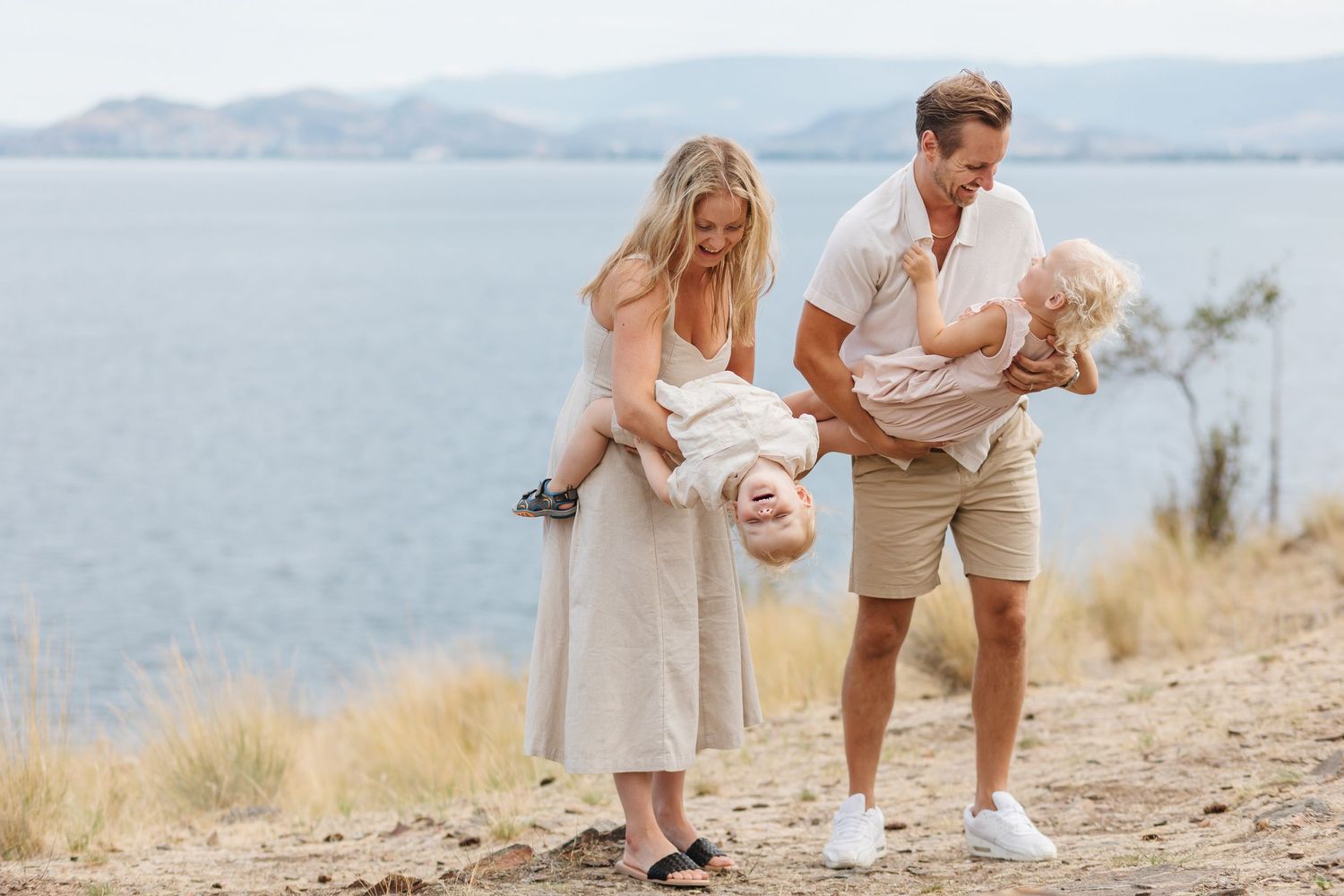 A family enjoys a playful moment together on a coastal path overlooking calm waters and distant mountains.