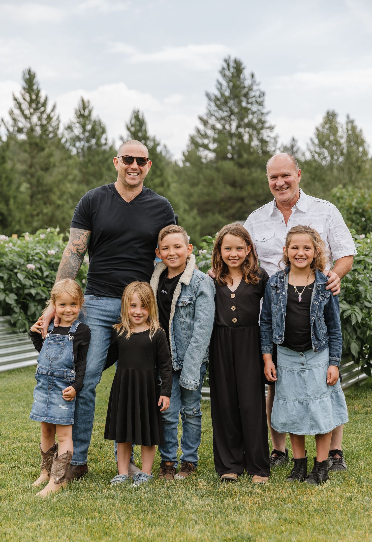 A series of five casual outdoor family photos showing a group in coordinated black and denim outfits on grassy lawn.