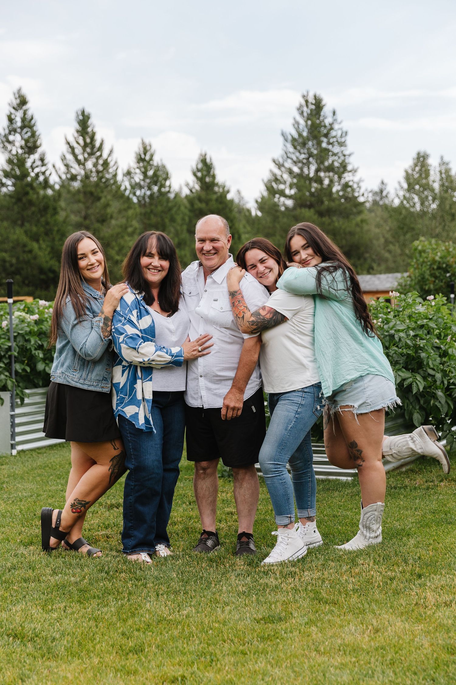 A playful group poses together on grass with white fencing and evergreen trees in the background.