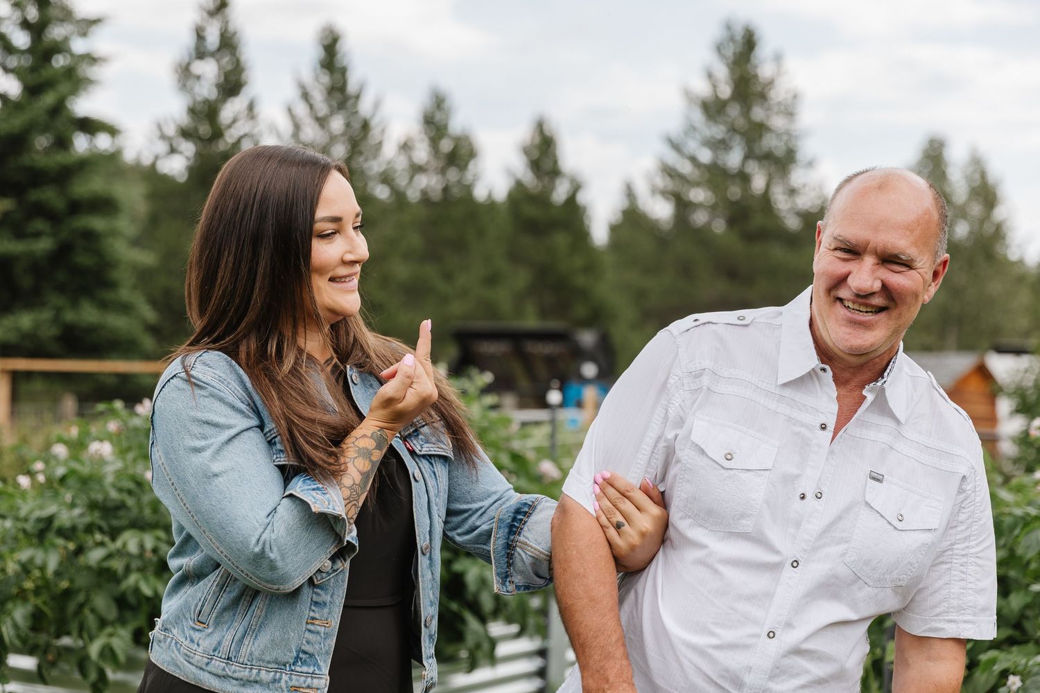 A couple shares joyful laughter during an outdoor photo session in a garden setting.