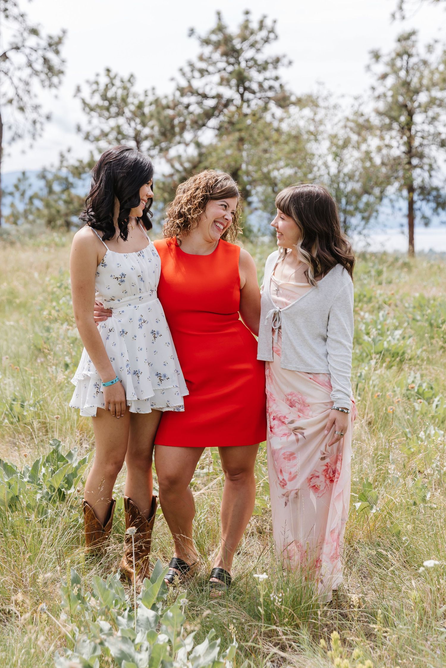 Three friends in red and white outfits laugh together while standing in a sunny wildflower meadow.