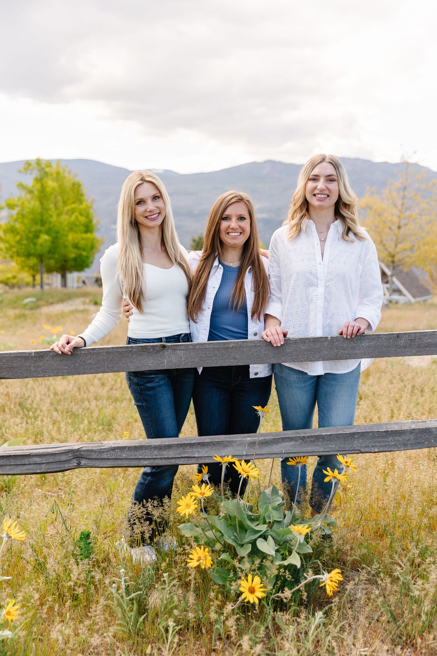 Group leaning against wooden fence with yellow wildflowers blooming below during family photoshoot in West Kelowna at sanctuary gardens