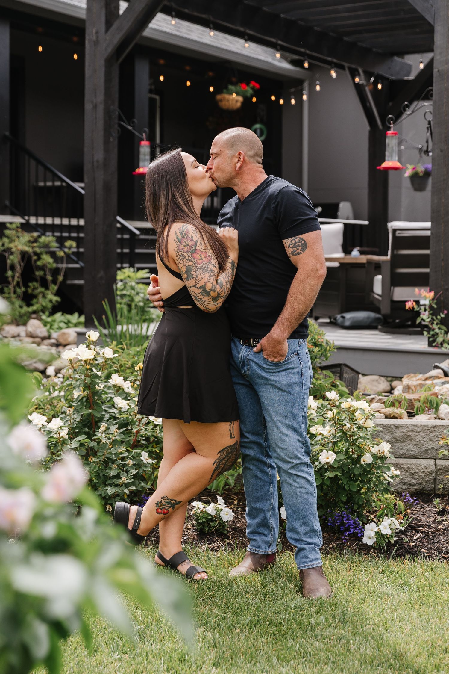 A romantic couple shares intimate kisses in a garden setting with string lights and flowers in the background.