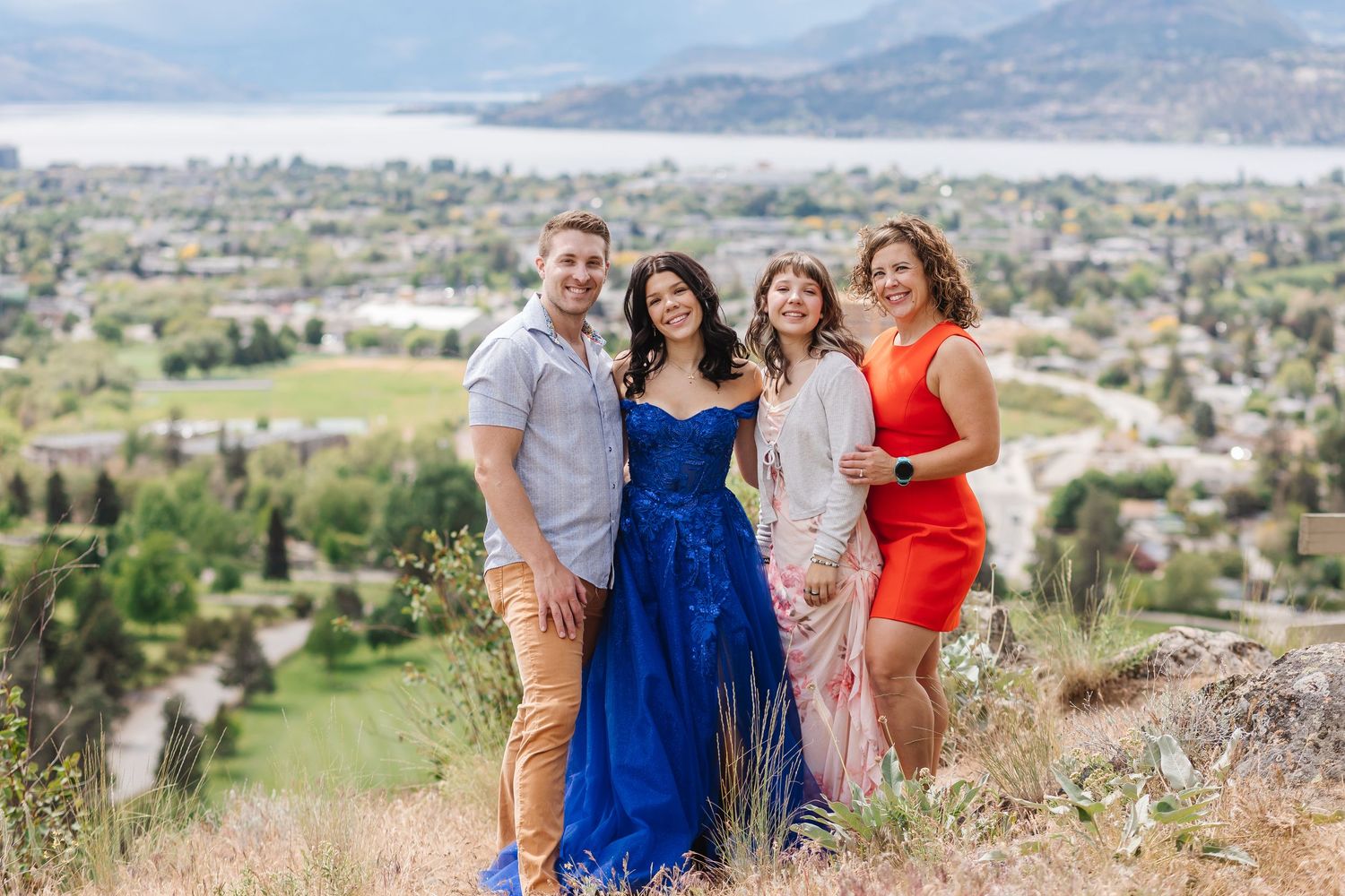 A group in blue and red outfits poses together on a hilltop overlooking a scenic valley landscape.