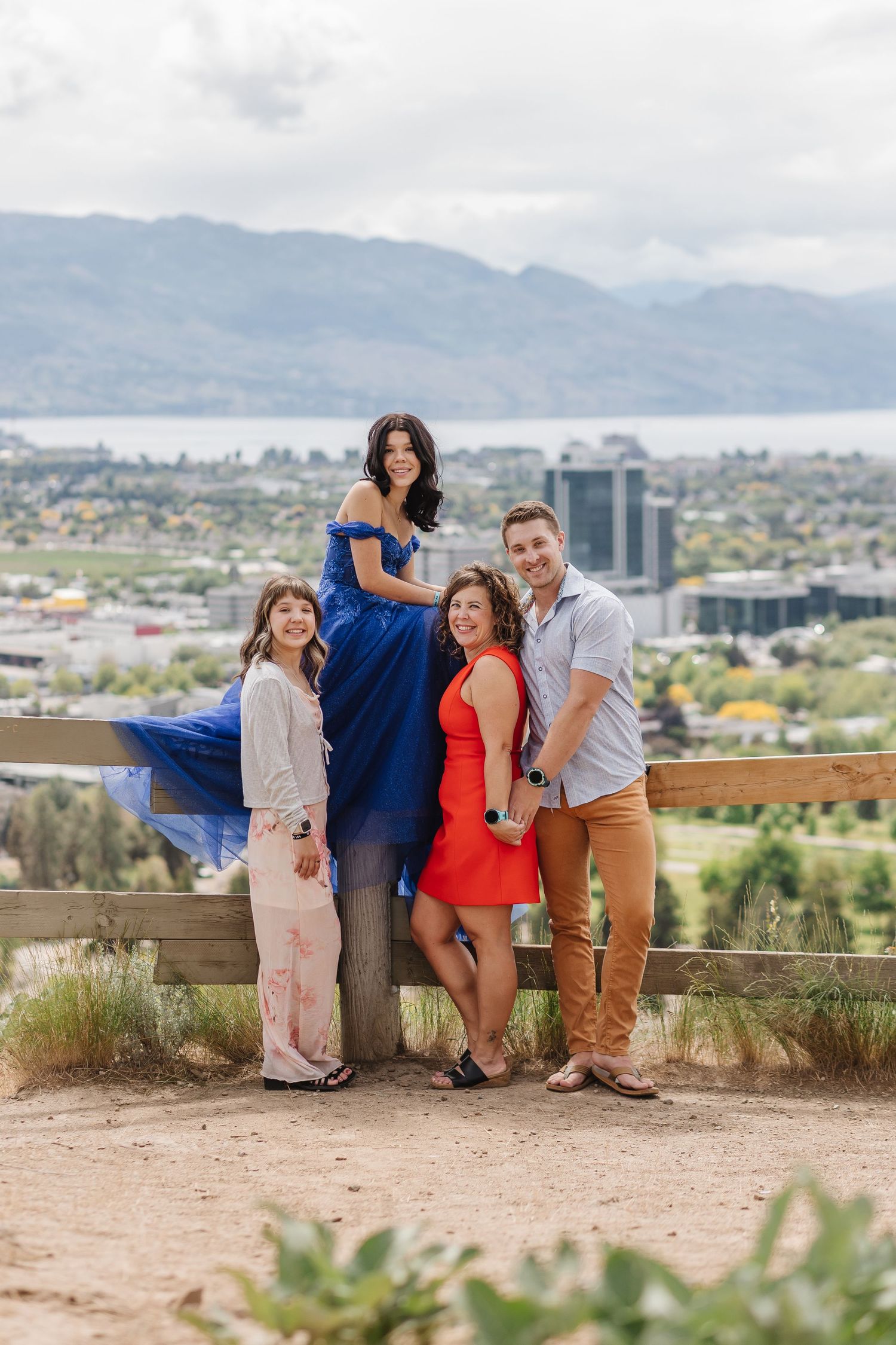 A group poses playfully for photos on a hilltop overlook with mountain views and city buildings in the background.