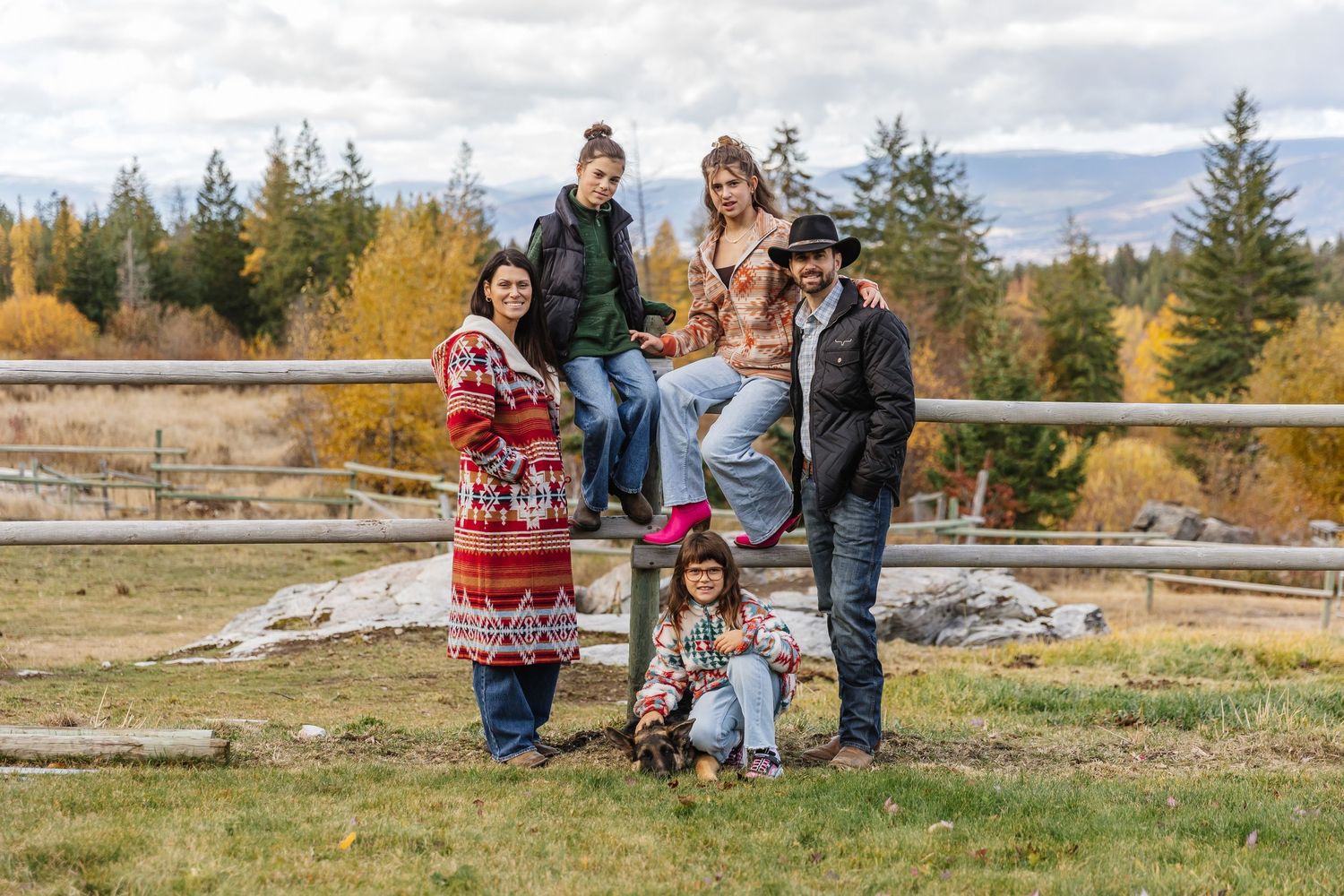 Family enjoying a scenic autumn walk along a rustic wooden fence with colorful fall foliage in the background.