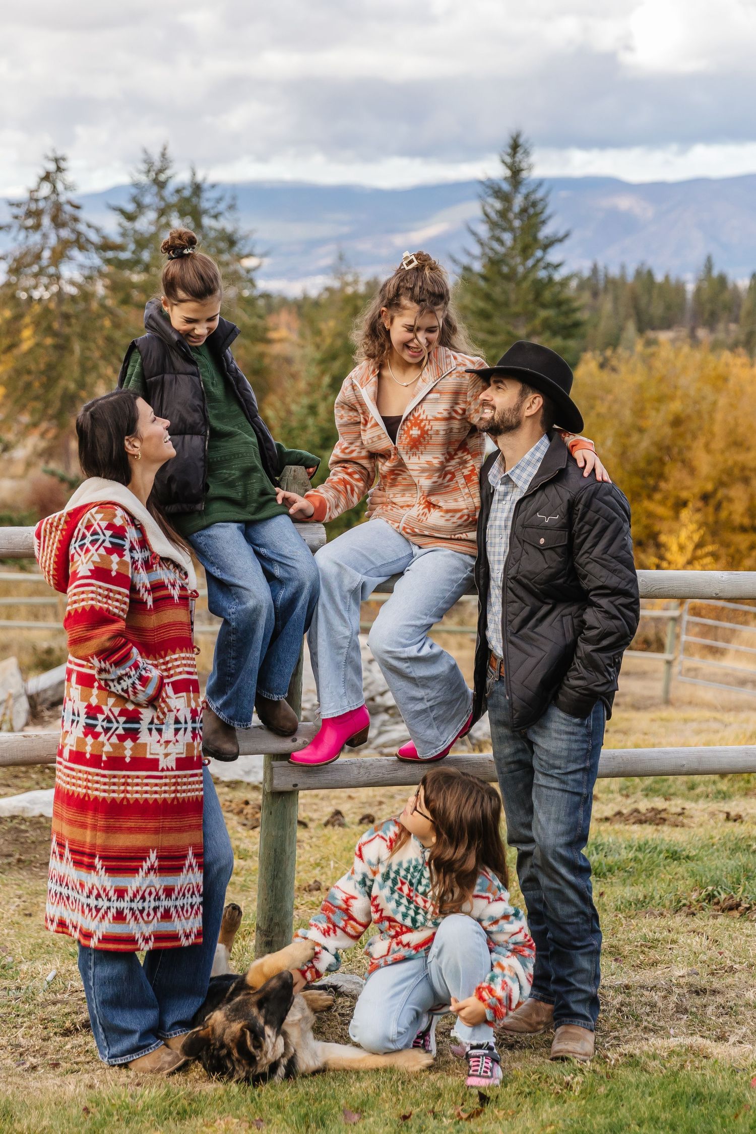 A family shares joyful moments together outdoors during a fall photo session in front of evergreen trees.