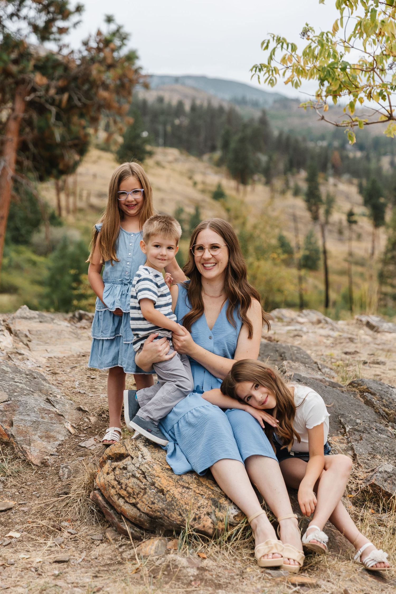 A group in coordinated denim and blue outfits sits together on rocky terrain with mountains in the background.