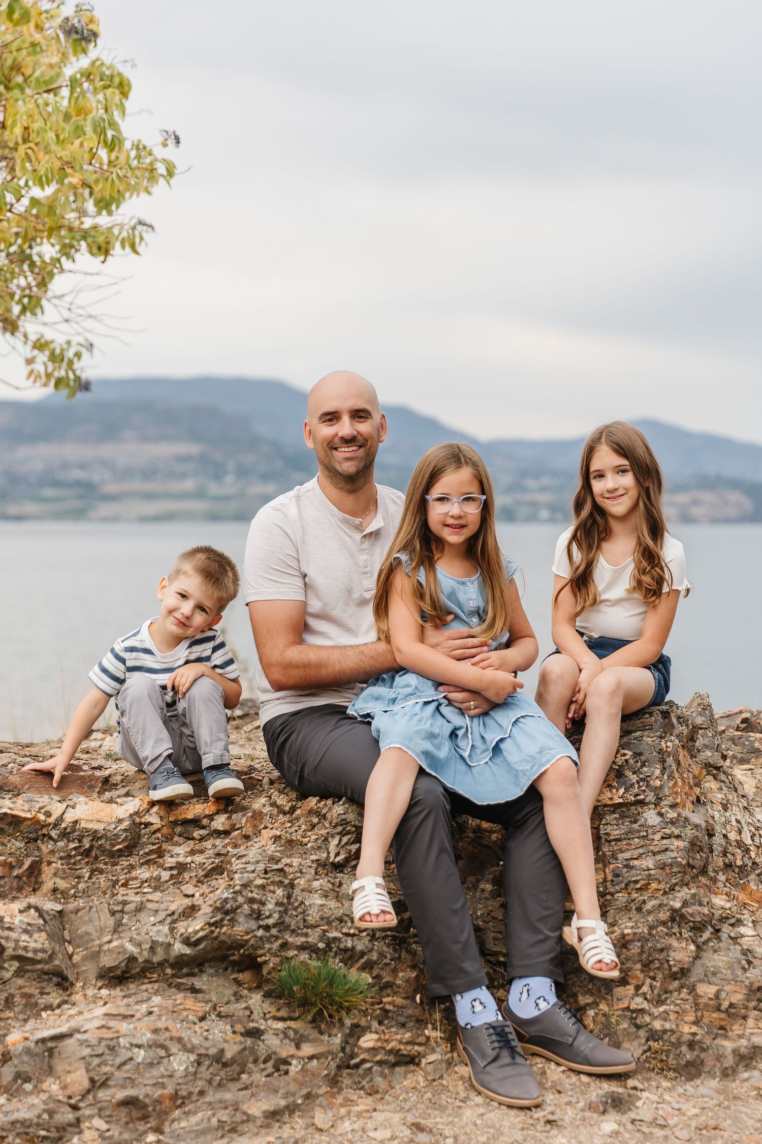 A family sits together on a rocky outcrop overlooking a scenic mountain lake on a cloudy day.