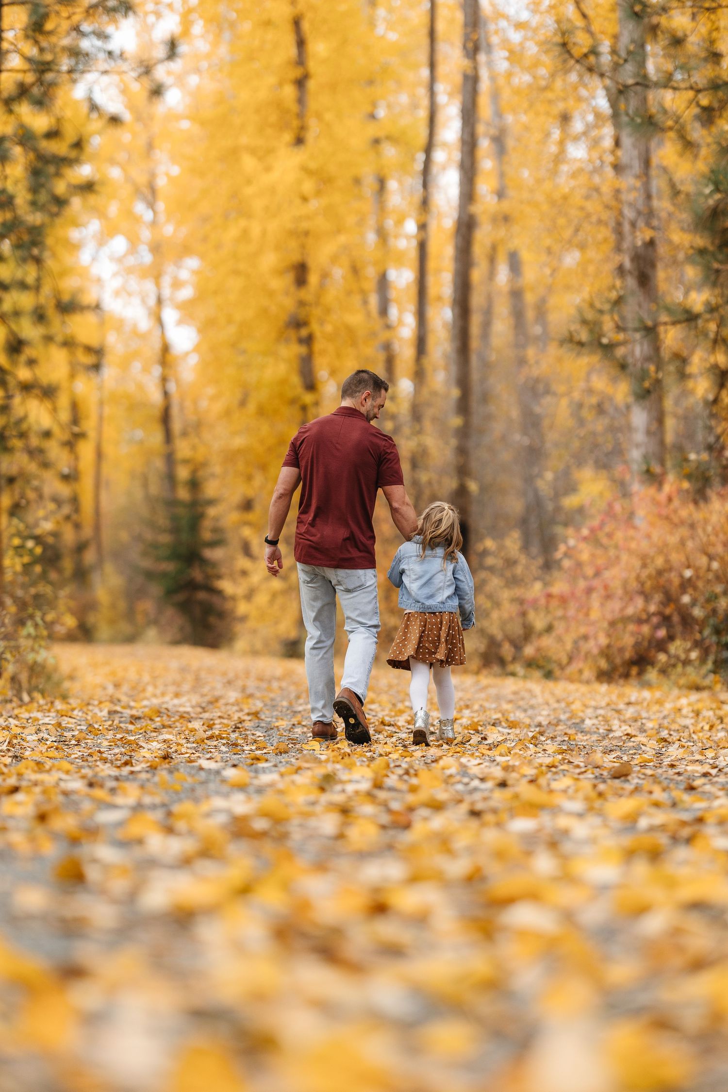 People walking together on a path covered in golden autumn leaves with sunlit trees in the background.
