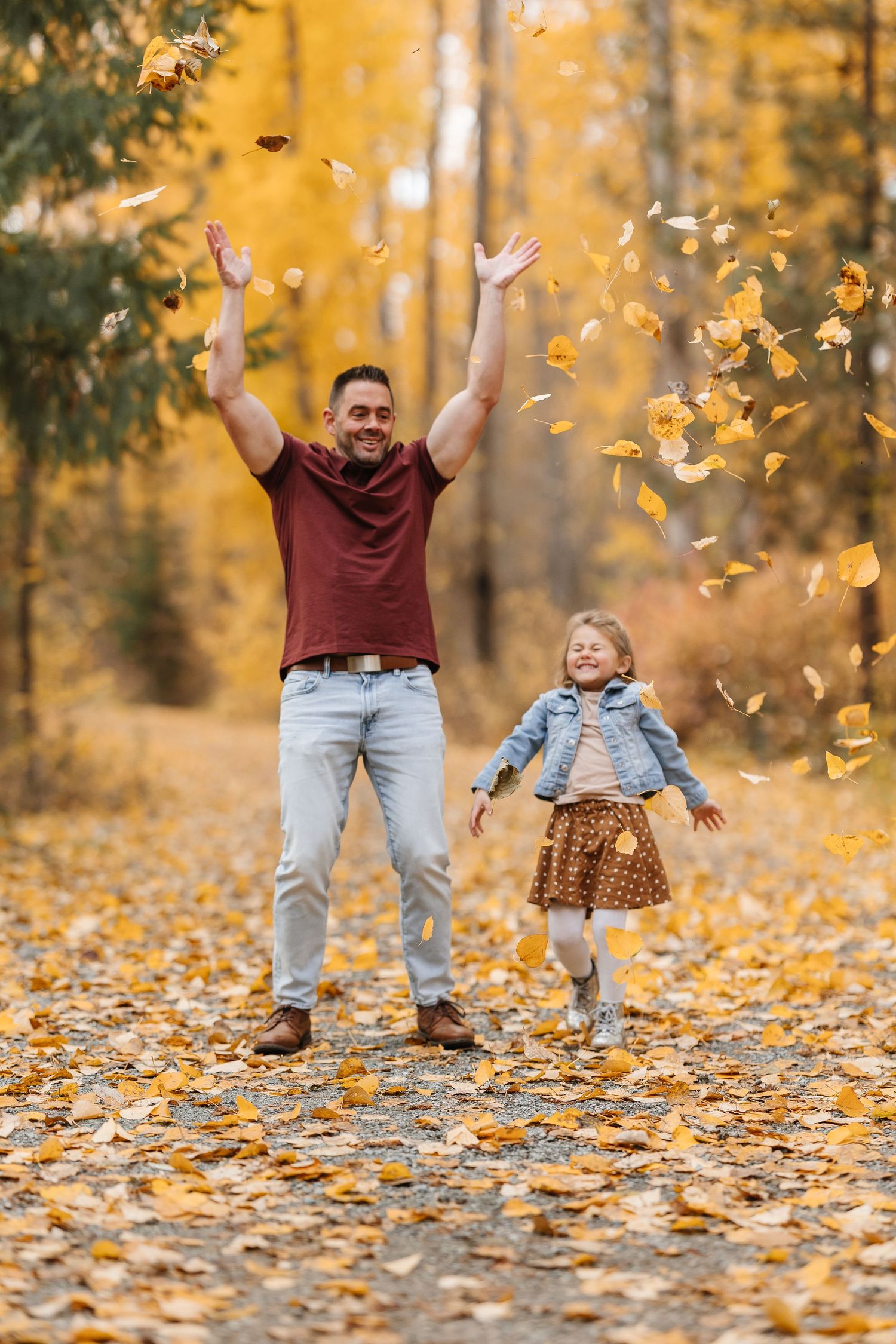 People playing in autumn leaves throwing yellow and orange foliage into the air during a fall photoshoot.
