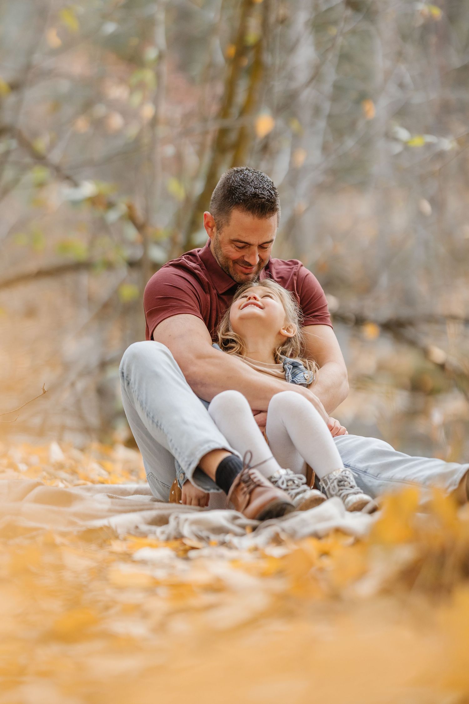 Parent and baby lying on autumn leaves sharing a tender moment in a park setting.