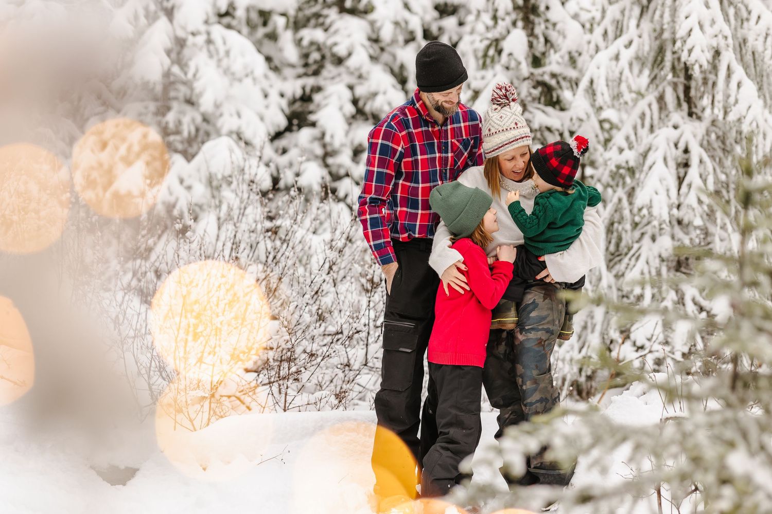 A couple embraces in a romantic winter scene surrounded by snow-covered evergreen trees at sunset.