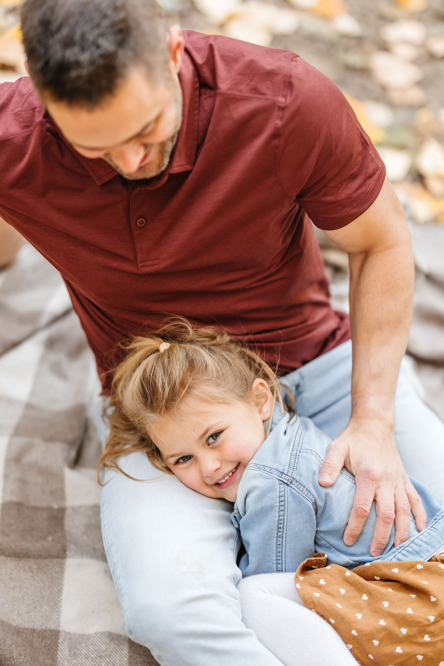 A playful moment captured on a blanket outdoors as a child in denim giggles while being tickled.