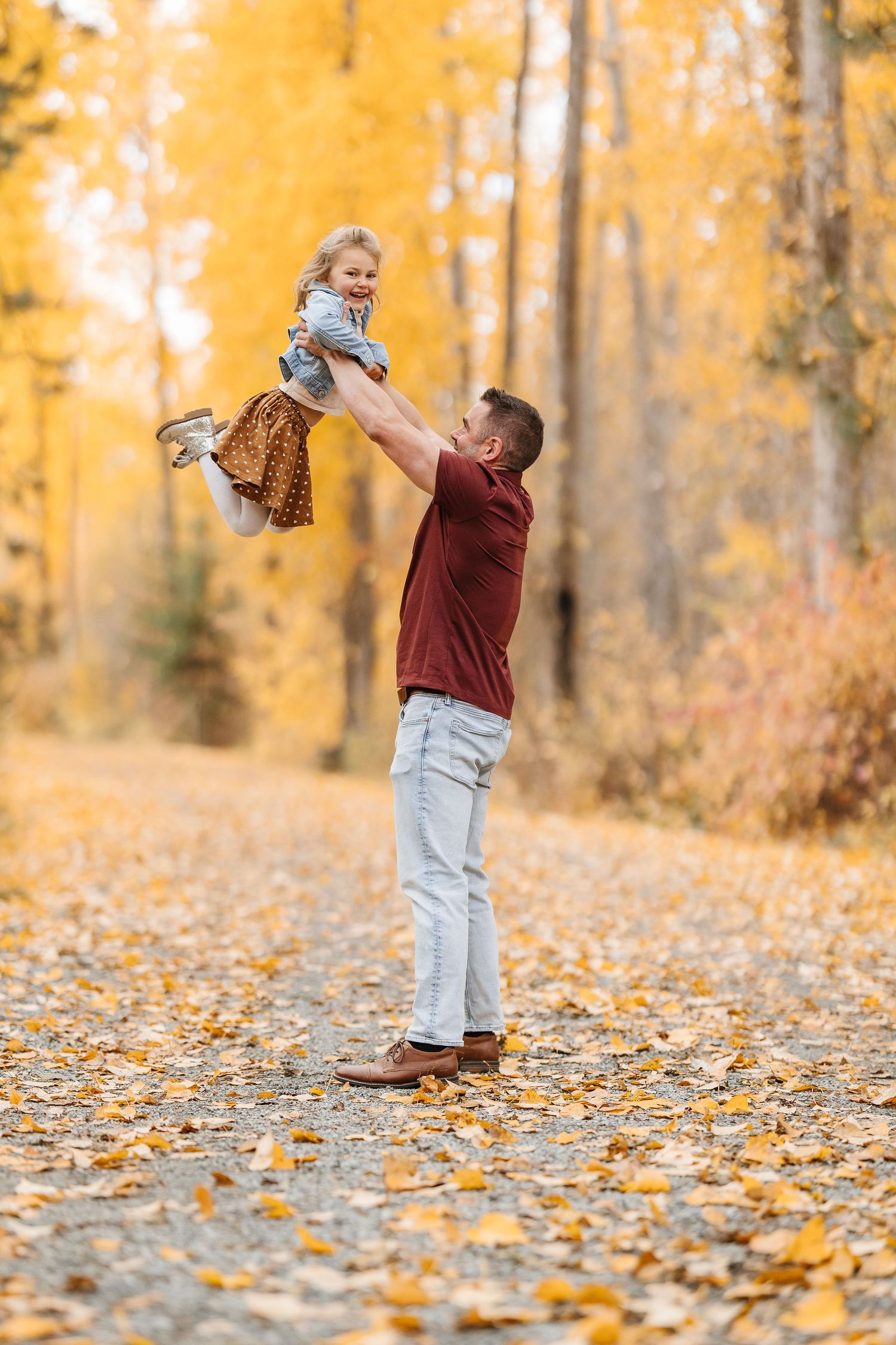 Parent playing with baby among golden fall leaves in a sunlit forest.