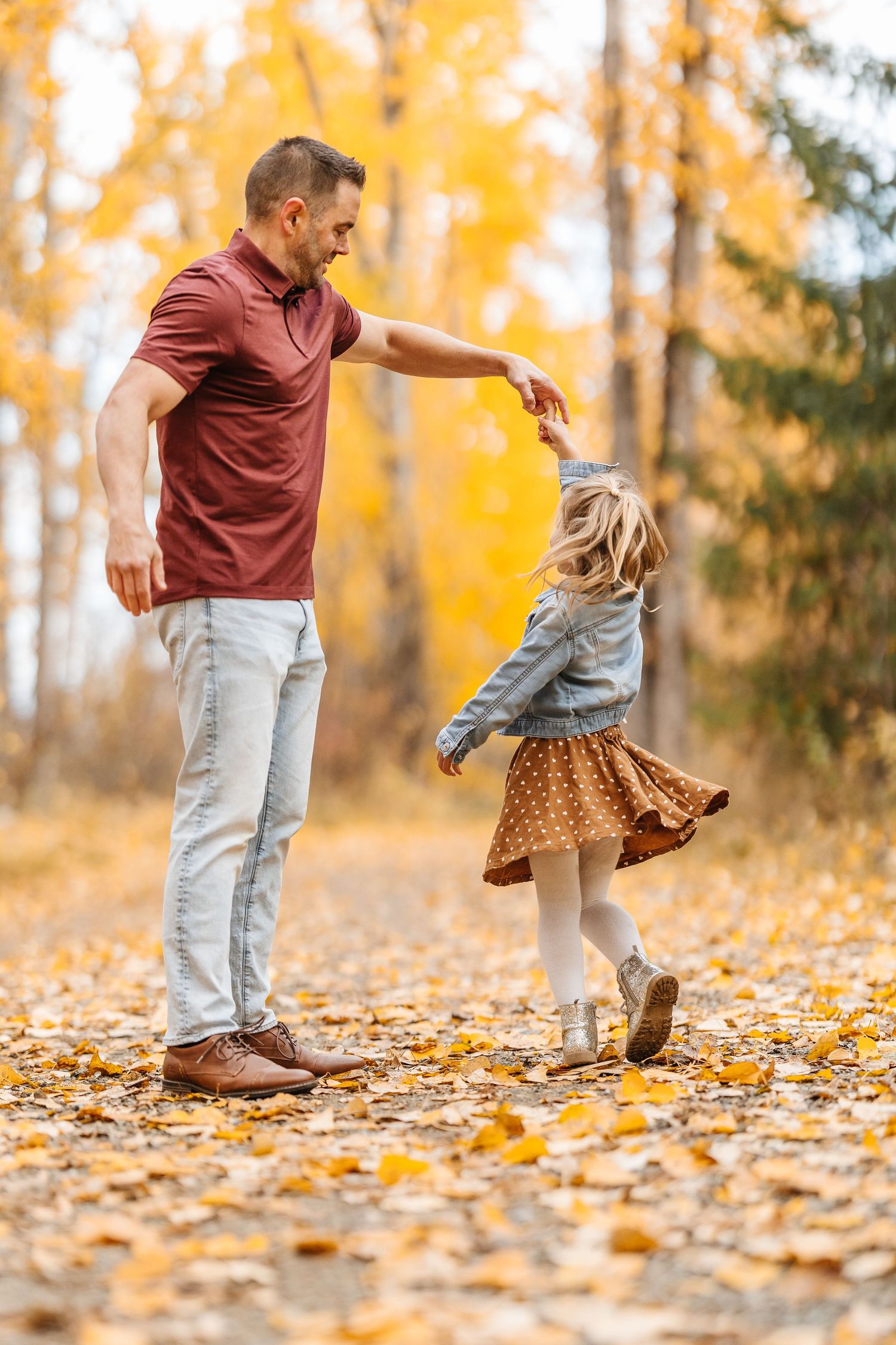 Dancing and playing in fallen autumn leaves on a forest path surrounded by golden foliage.