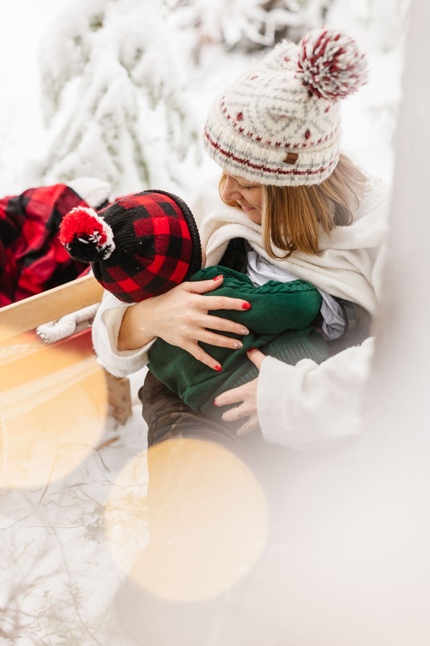 Person wearing a cozy winter knit hat and white sweater wraps Christmas presents on a light wooden surface.