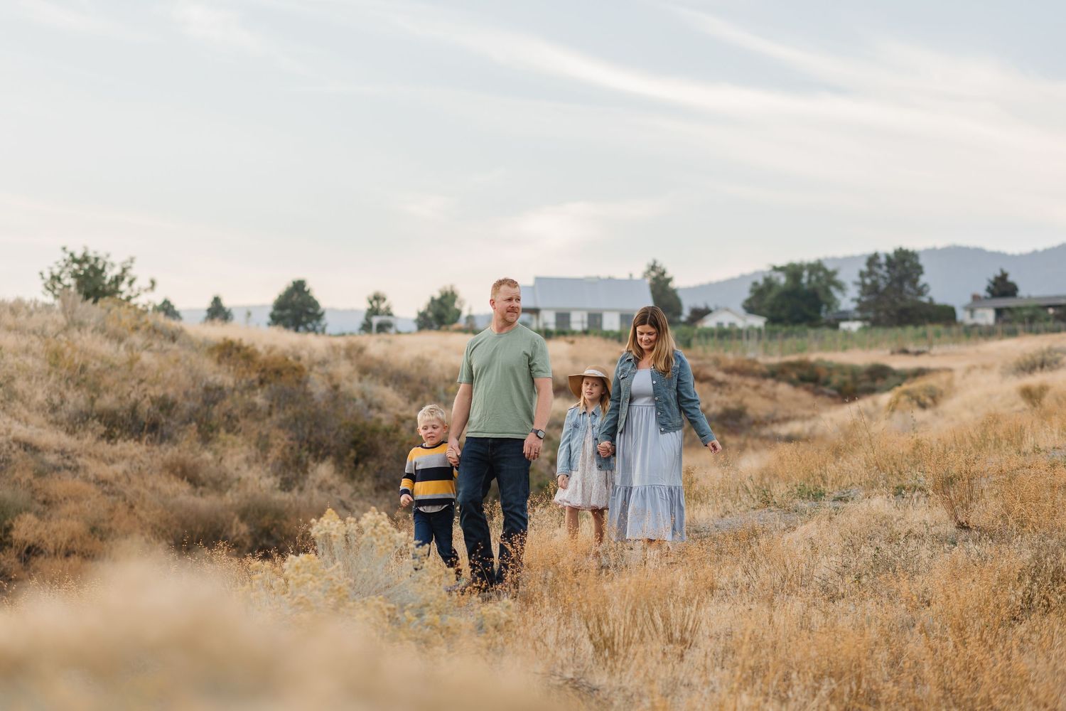 A couple walks together through a golden field at sunset with mountains in the background.