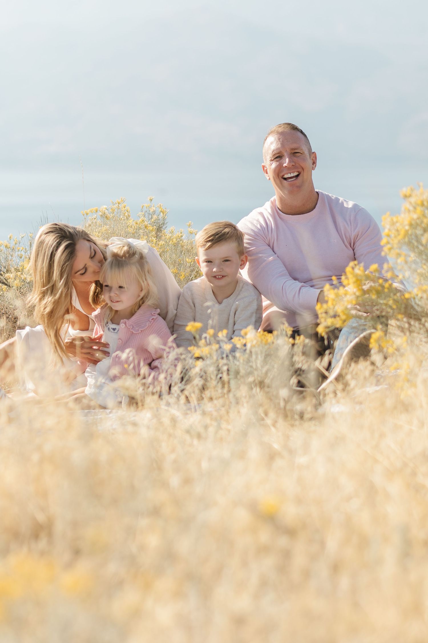 A family sits together in a golden field of tall grass and wildflowers on a bright autumn day.