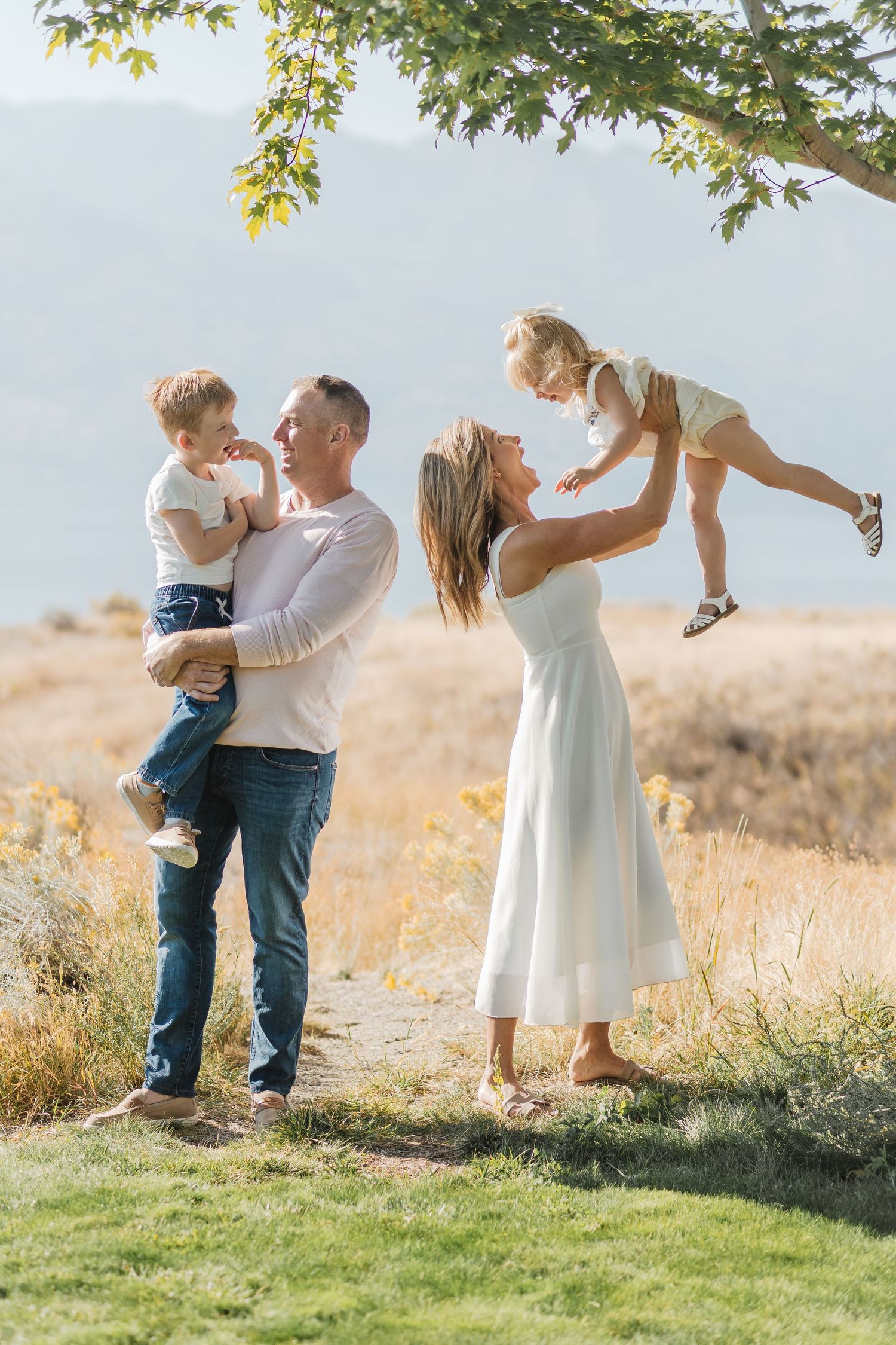 Family enjoying a tender moment together outdoors in a sunlit field with green grass and golden light.