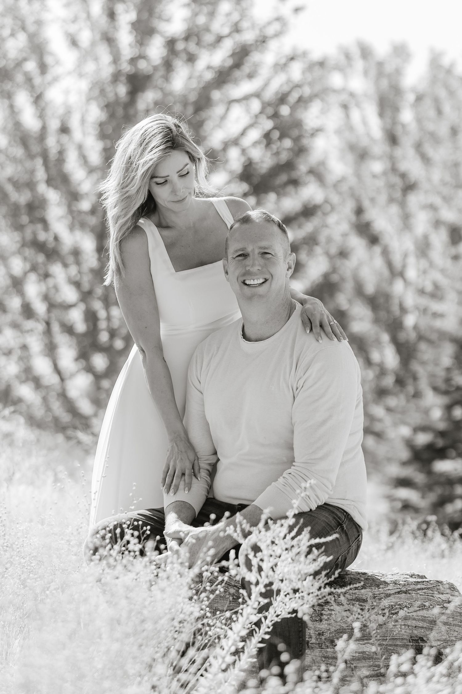 Black and white portrait of couple embracing in a dreamy meadow setting with soft natural lighting.