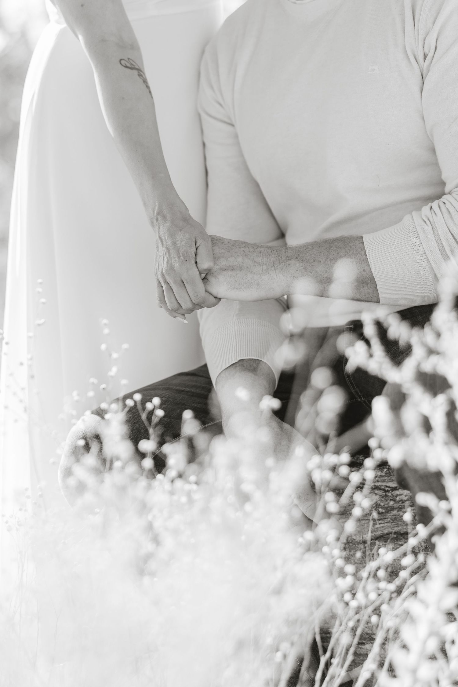 A black and white wedding photo showing two people standing together with soft bokeh lights in the foreground.