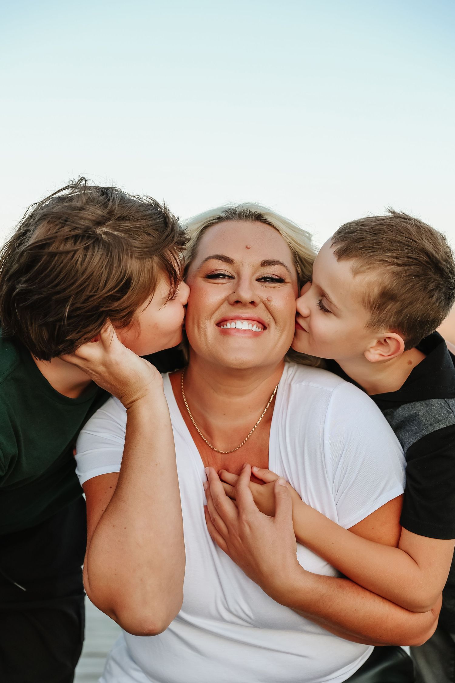 An affectionate family photoshoot moment captured against a light blue sky background in West Kelowna