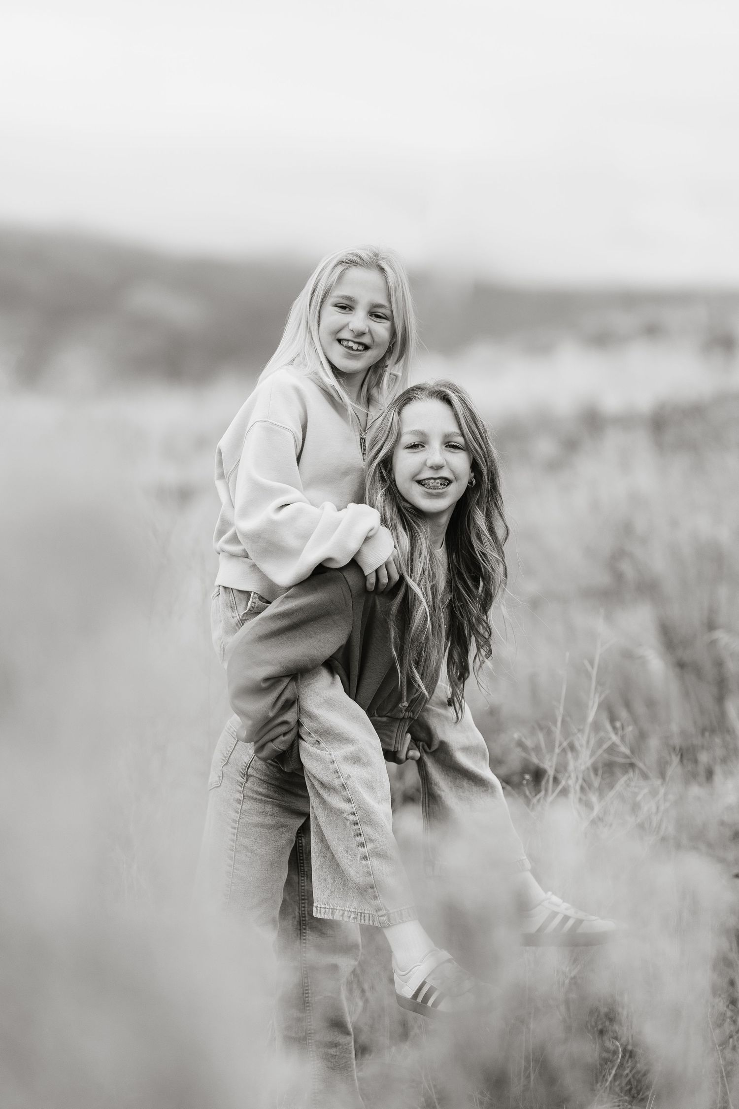 Black and white photos show a joyful moment captured in a grassy field with natural lighting and candid expressions.