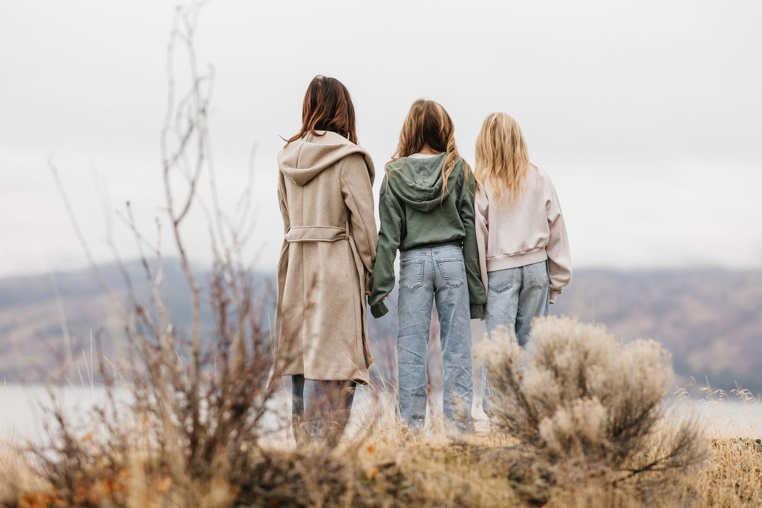Three people stand together overlooking a scenic mountain landscape while wearing casual outdoor clothing.