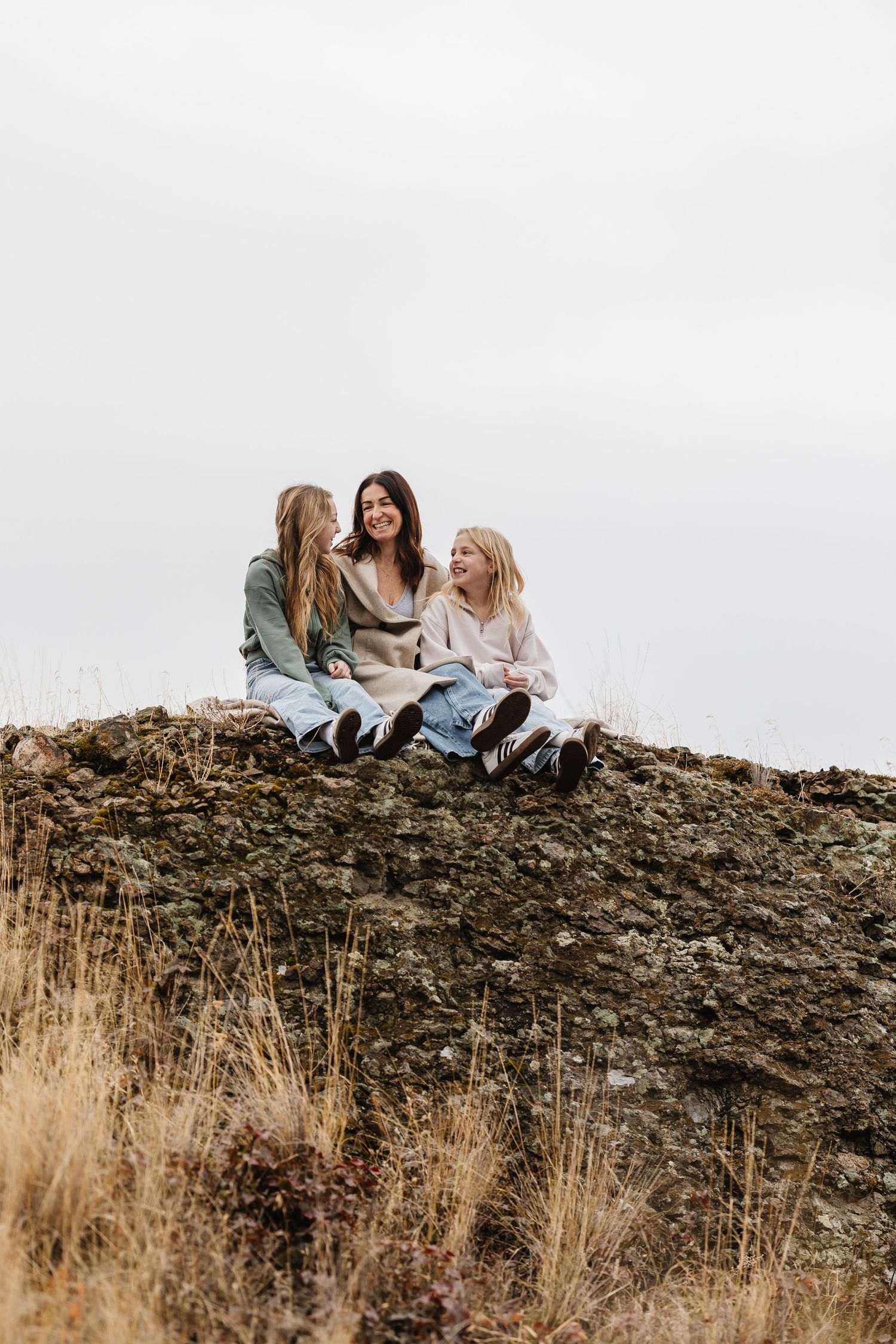 Three friends sitting together on a rocky hillside covered in dry grass during golden hour.