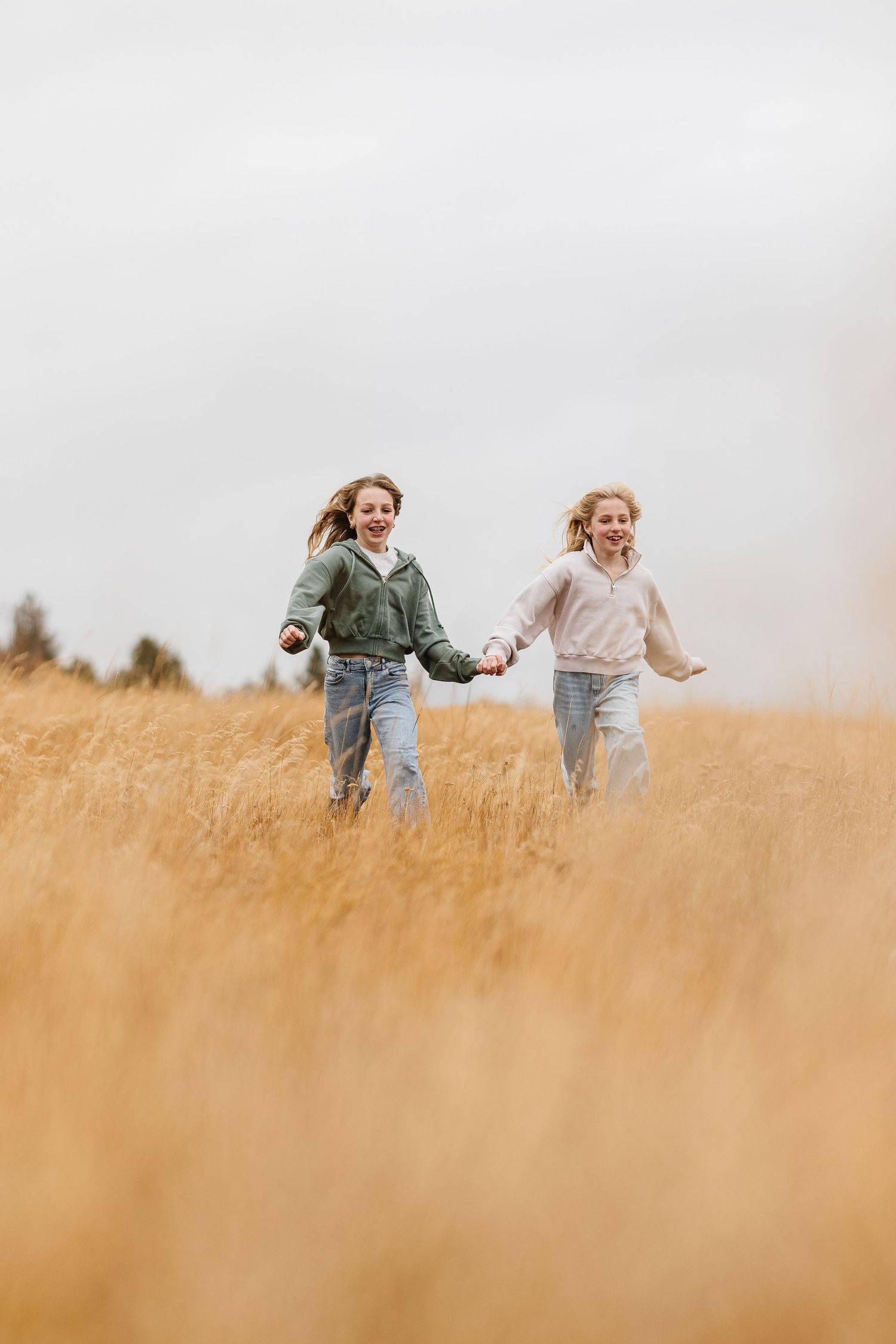 Three friends run joyfully through a golden wheat field on a cloudy summer day.