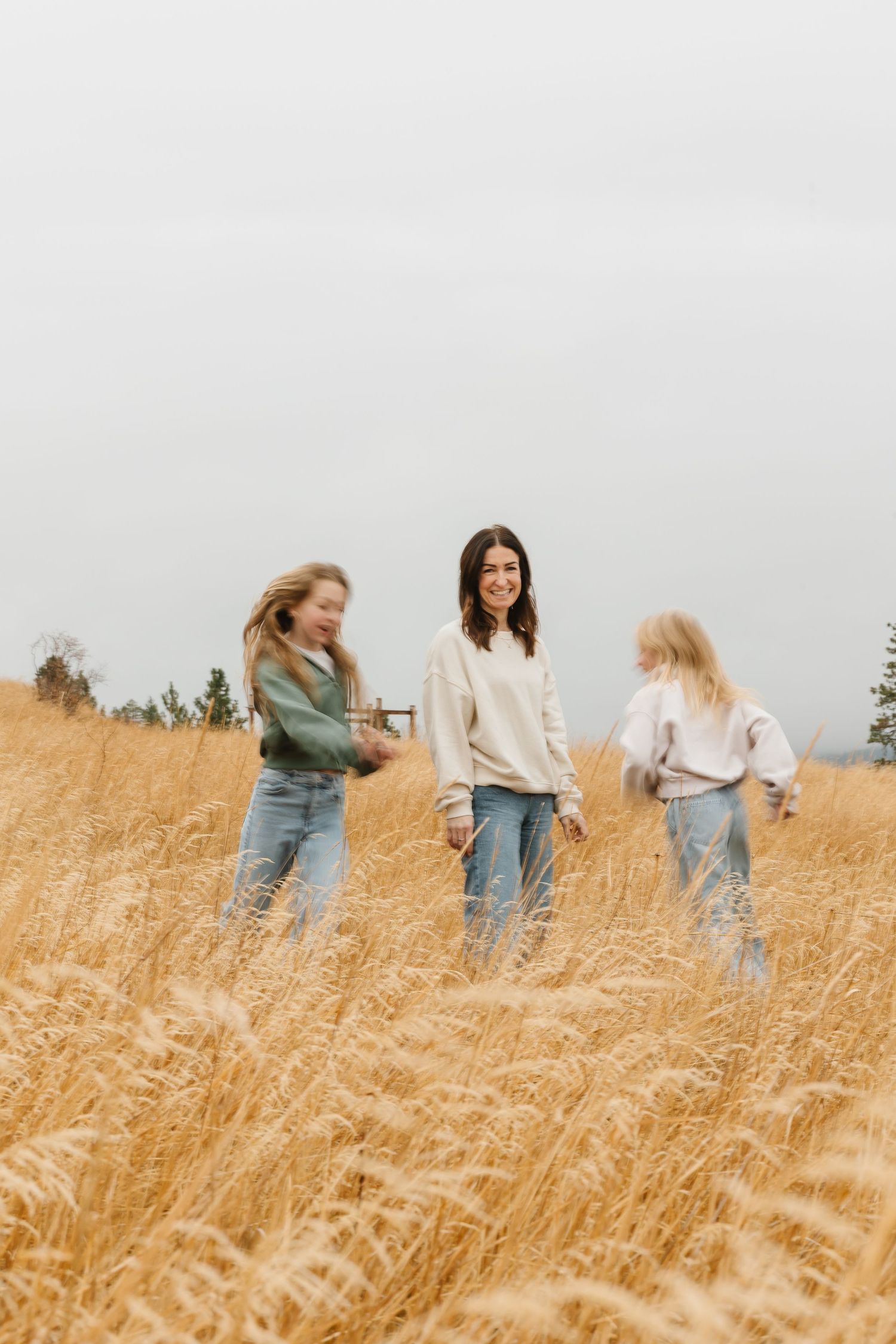 Three people standing together in a golden wheat field on an overcast day wearing casual clothing.