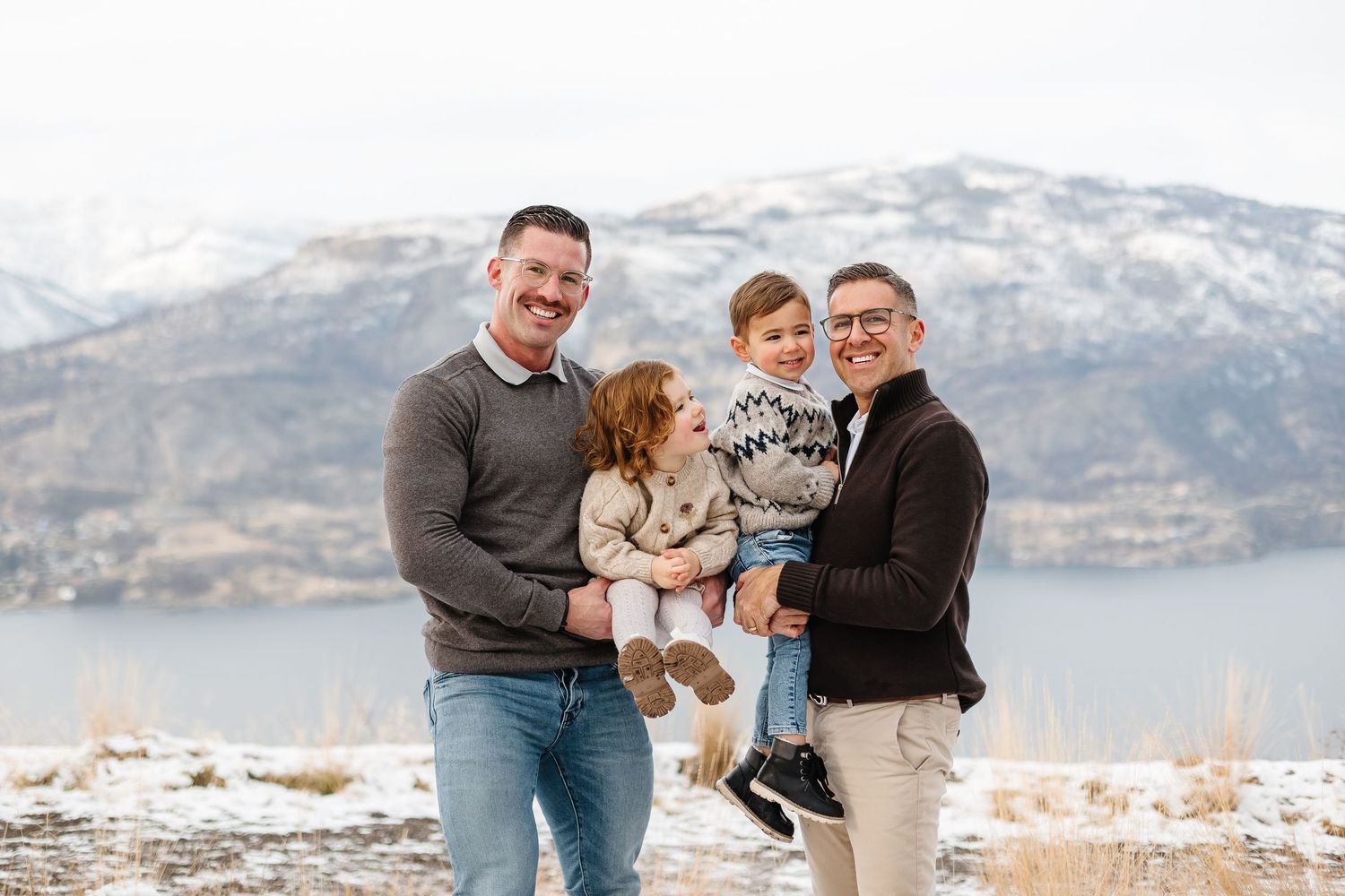 Playful winter family photoshoot with snow-capped mountains and lake in the background in kelowna