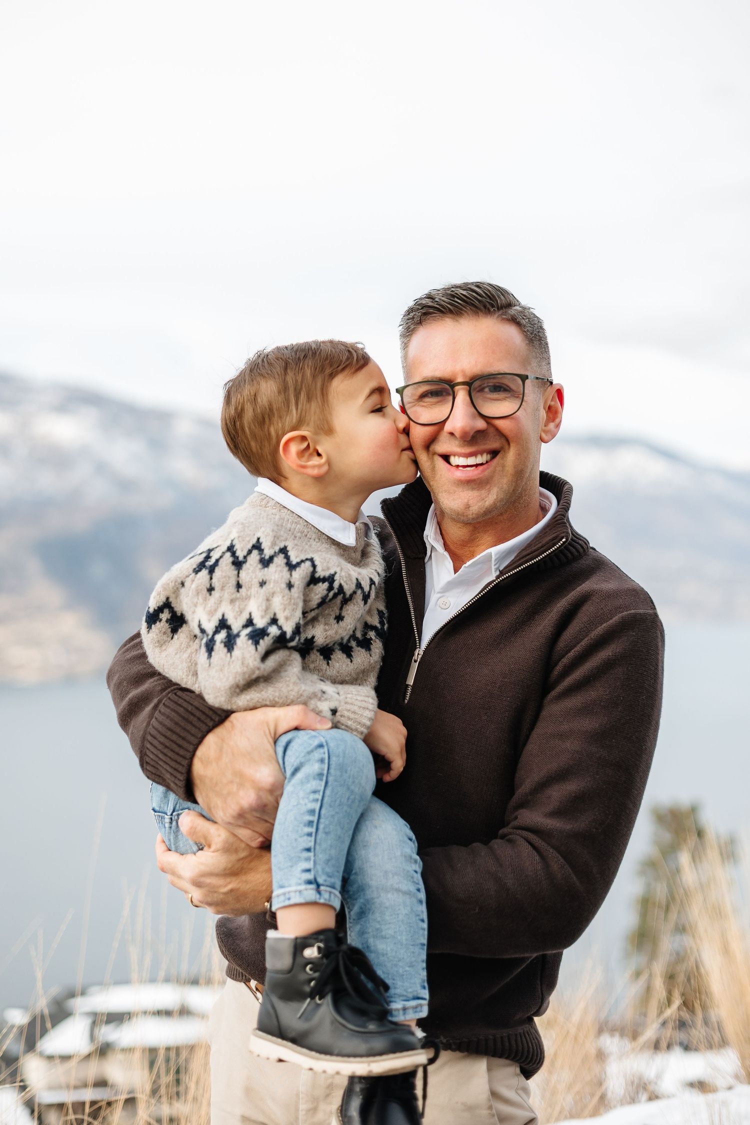 Candid moment of joyful interaction against a scenic winter mountain backdrop of okanagan lake in kelowna for family photoshoot