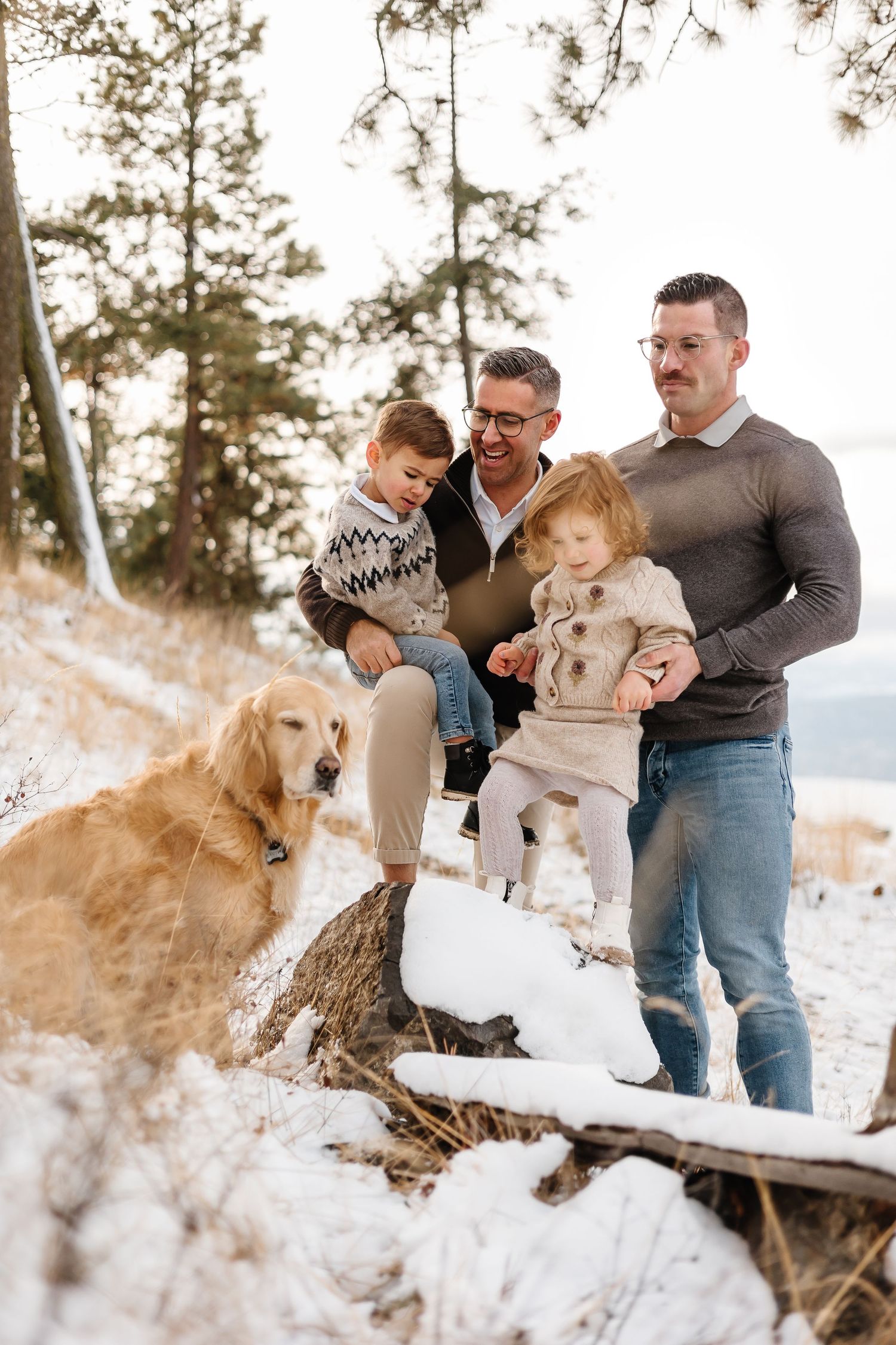 Family and their golden retriever playing together in the snow with mountain views in kelowna British columbia