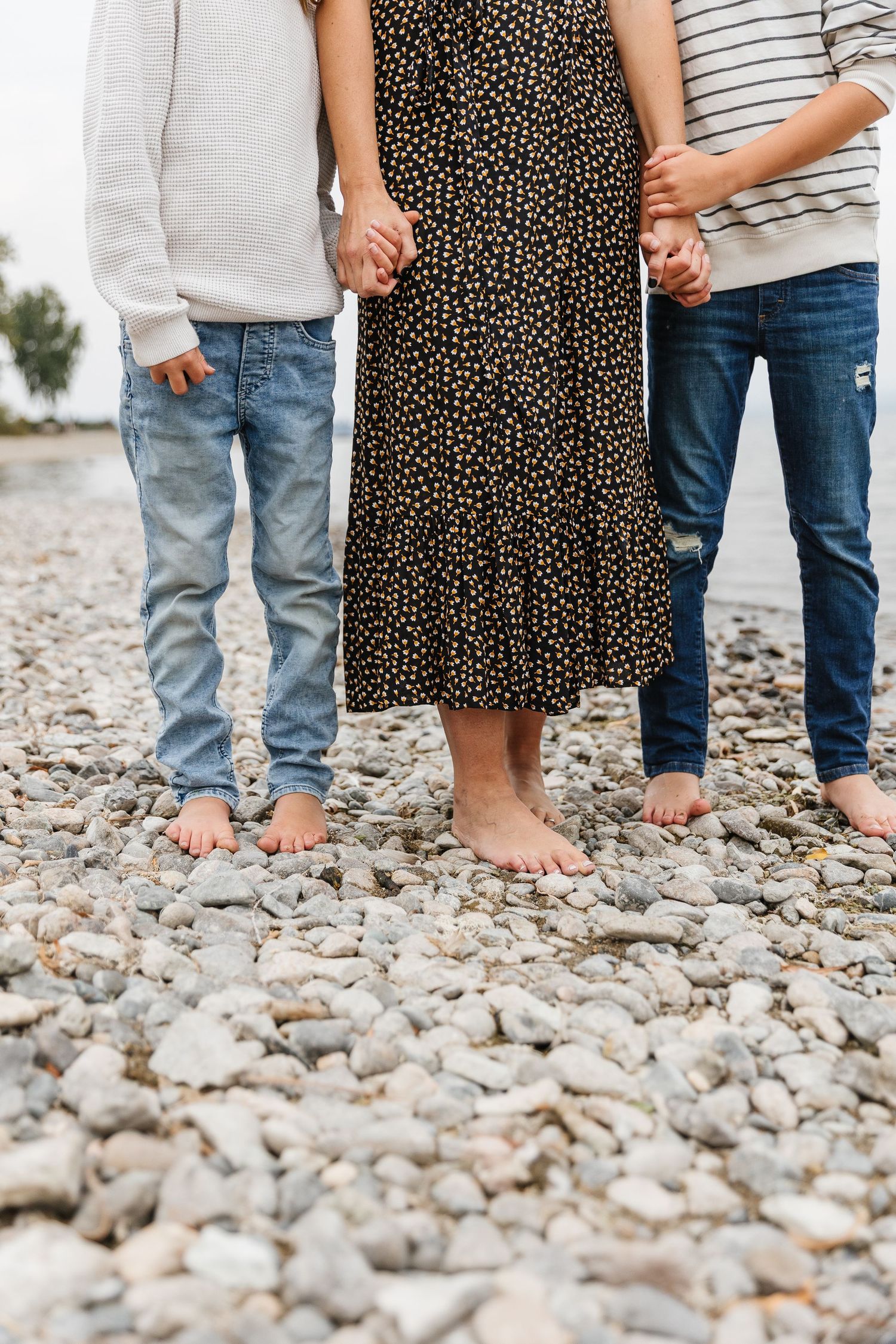 Close-up view of bare feet and denim-clad legs standing on a rocky beach surface.